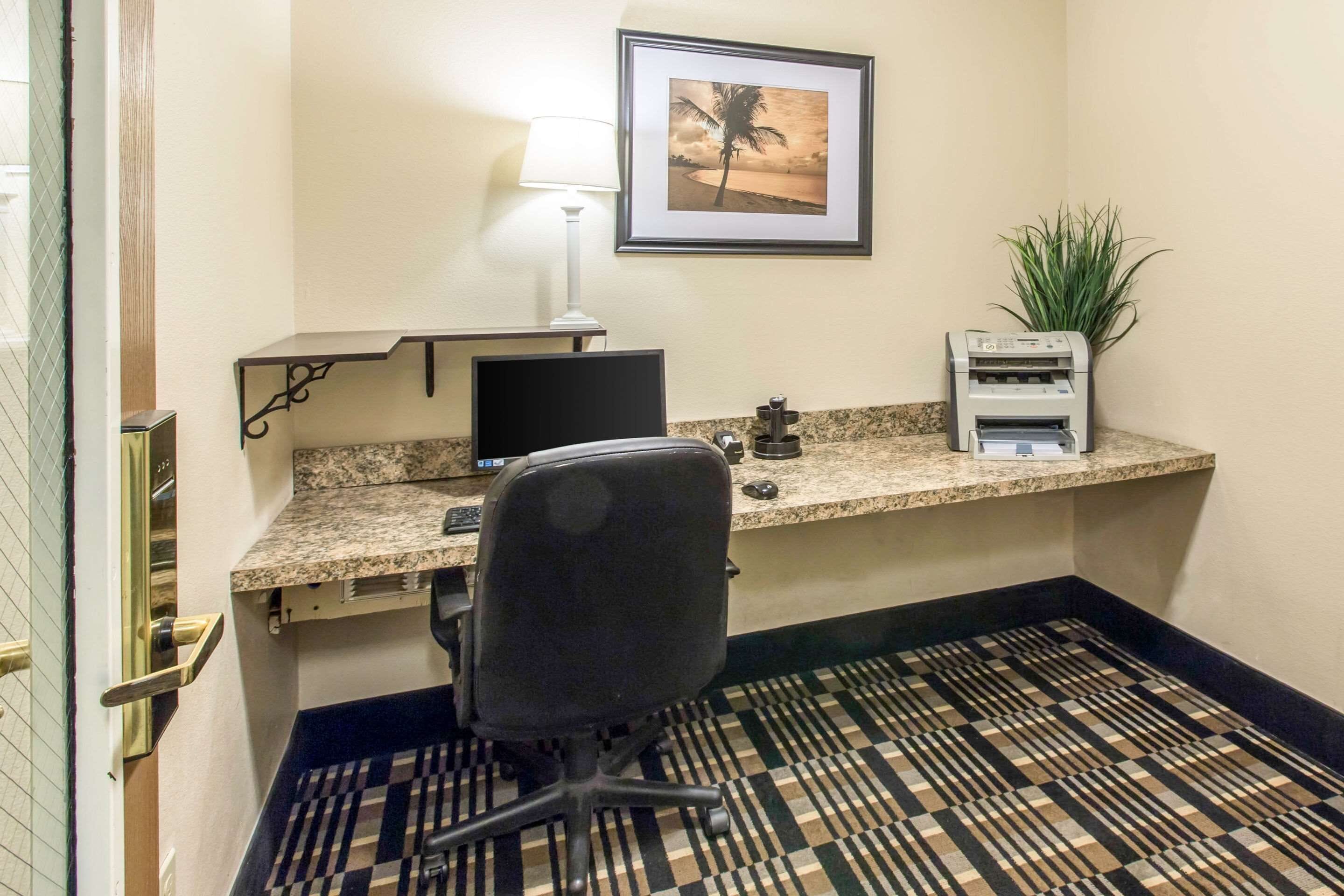 Une chambre d’hôtel équipée d’un bureau, d’un ordinateur, d’une chaise, d’une lampe, d’une imprimante et d’un tableau encadré au mur.