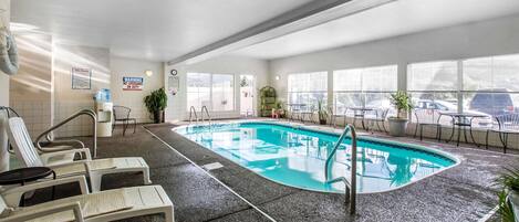 Una piscina interior con sillas de descanso, una escalera de piscina y ventanas amplias.