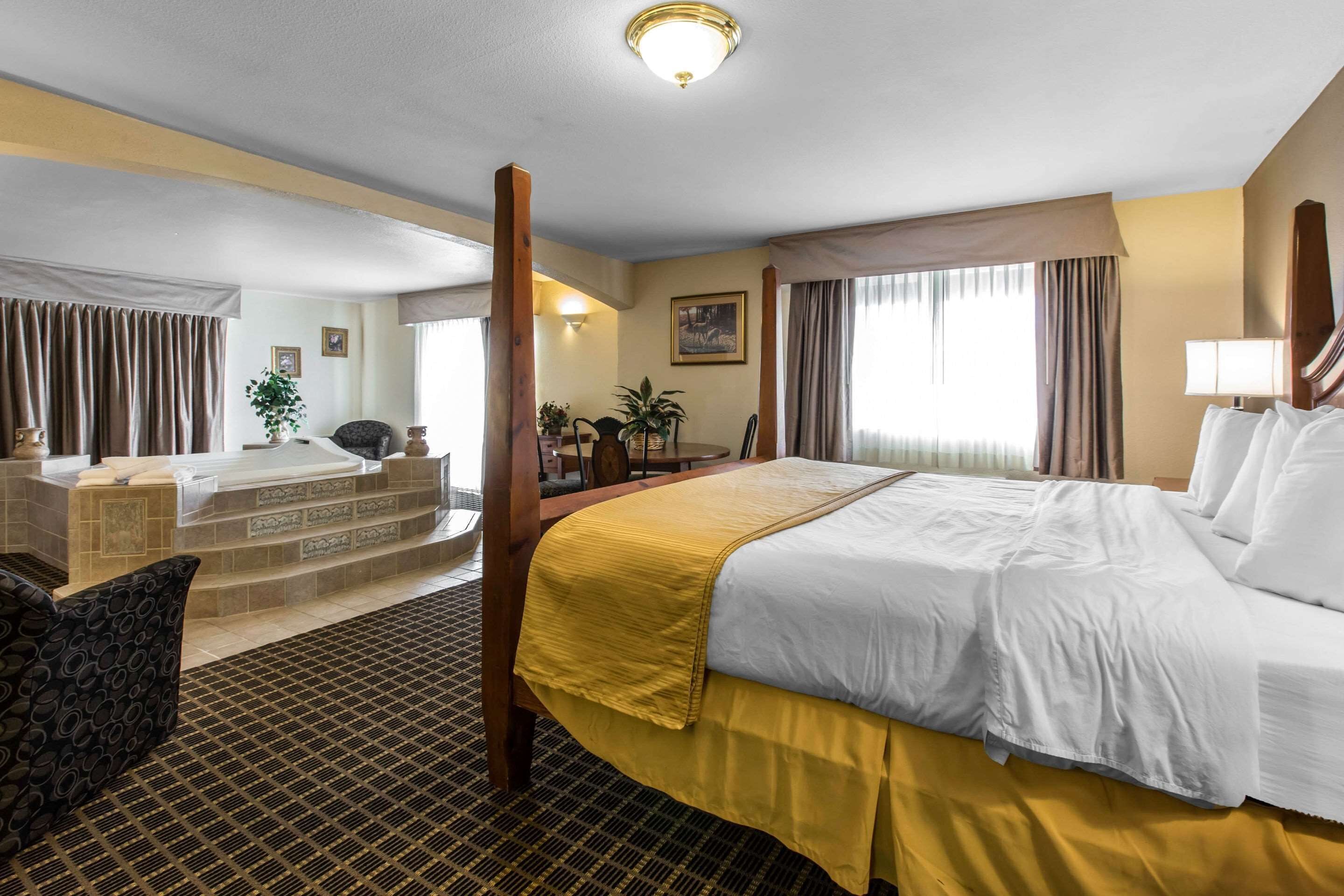 A hotel room with a large bed, a sitting area with a chair and a table, a bathtub, and a view of the outdoors.