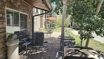 An outdoor patio with a stone wall, a grill, a trash can, and outdoor furniture.