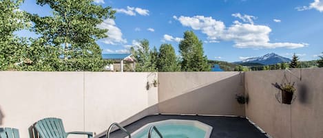 A rooftop pool area with two Adirondack chairs, a small hot tub, and a view of a mountain.
