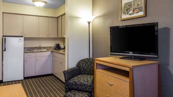 Una habitación de hotel compacta con kitchenette, un televisor de pantalla plana, un sillón estampado y una pequeña mesa de madera.