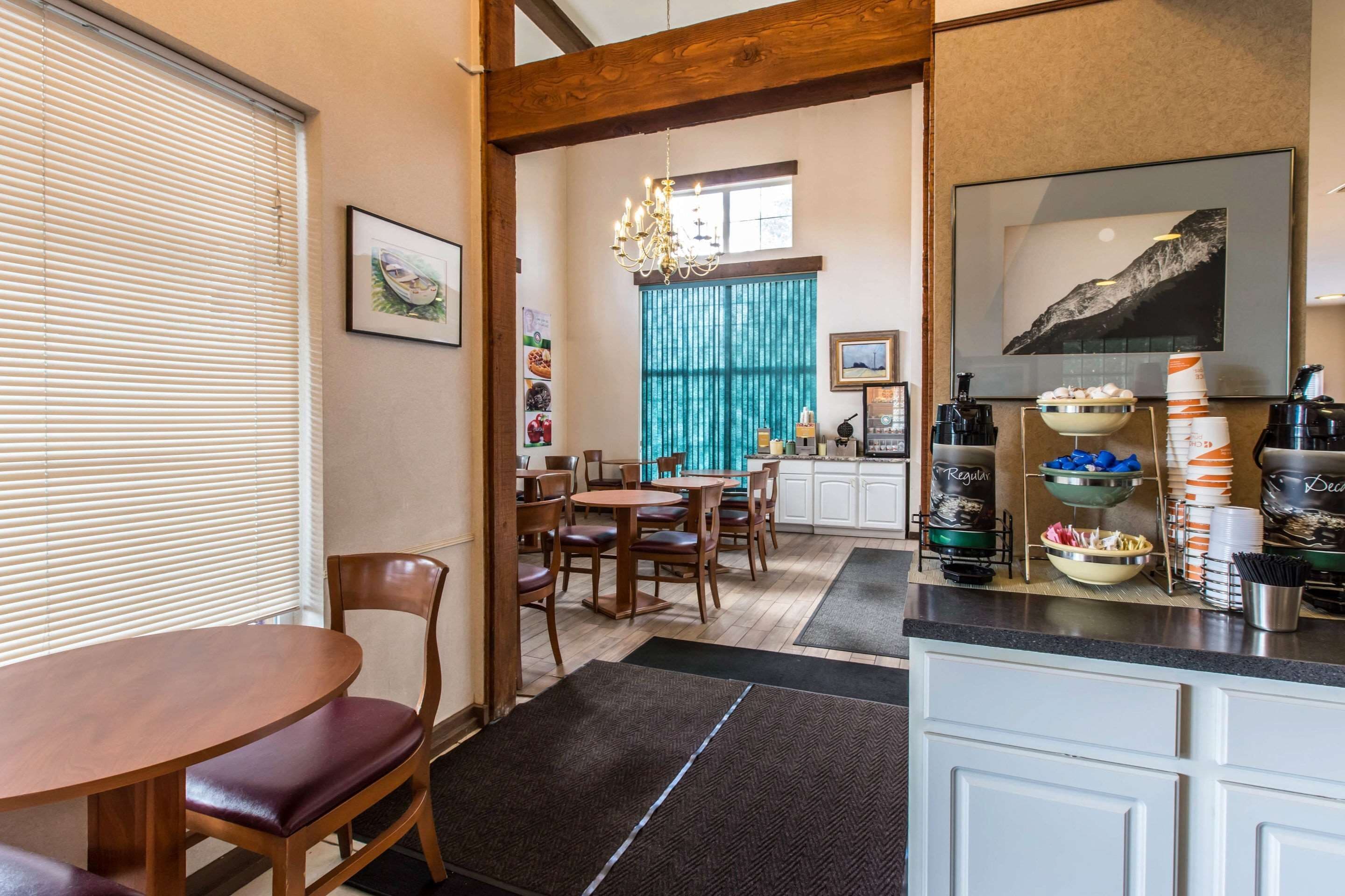 A dining area with a wooden table and chairs, a chandelier, and a kitchen area with a coffee station.