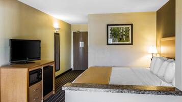 Habitación de hotel con cama, televisor sobre un mueble de madera, microondas, puerta y un cuadro en la pared.