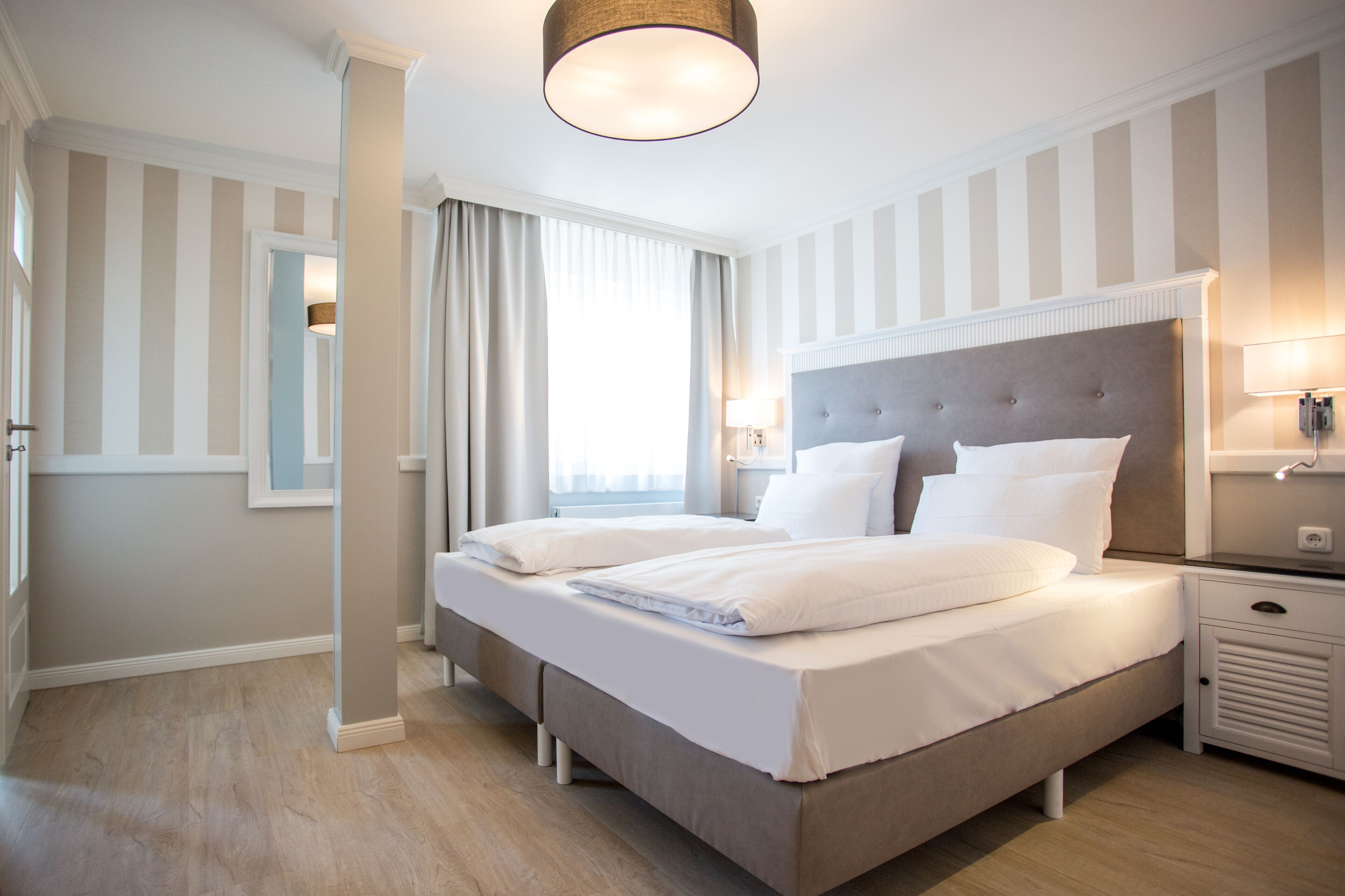 A double bed with a grey headboard, a bedside table with a lamp, and a window with curtains.