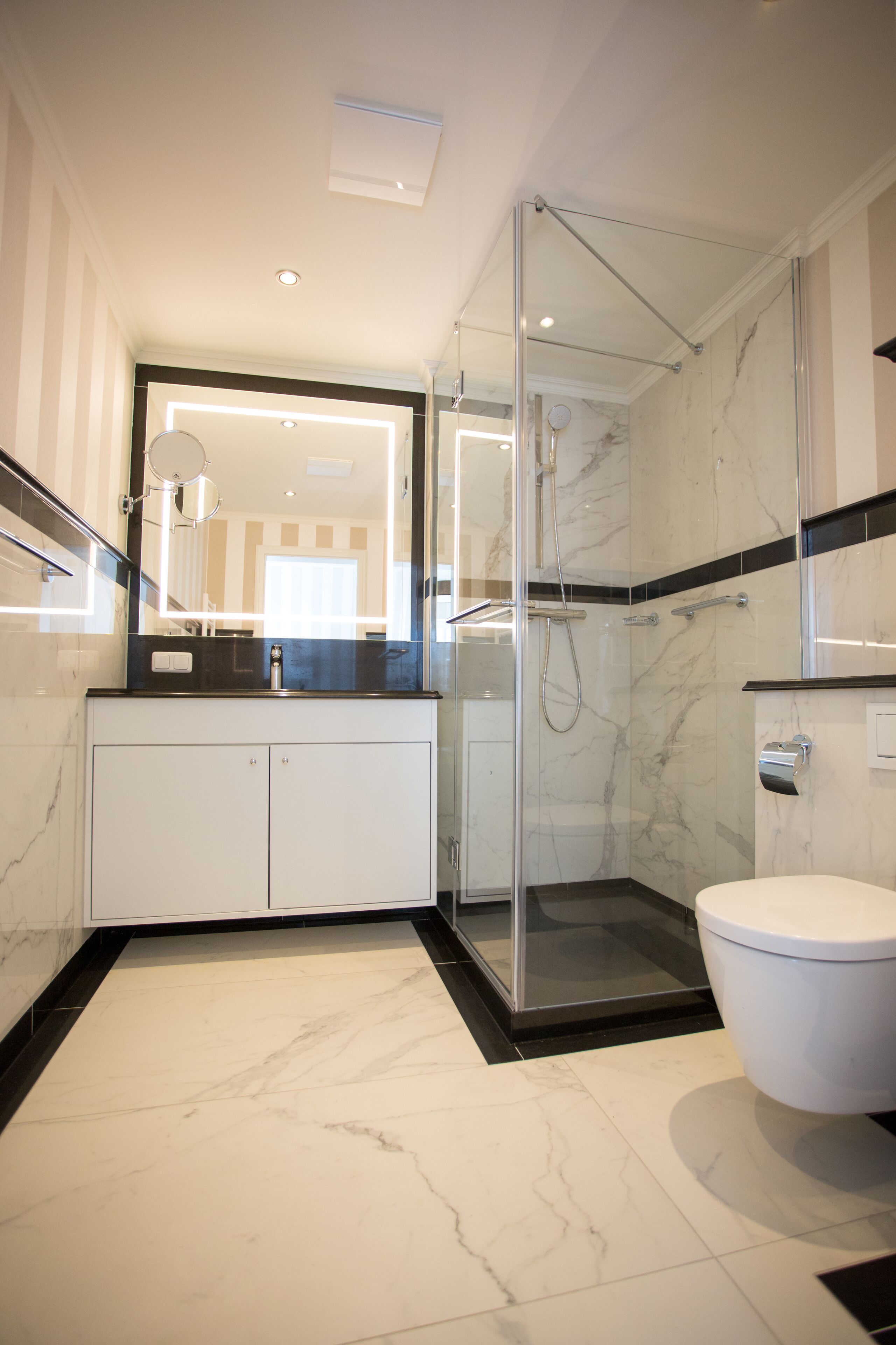 A modern bathroom with a glass-enclosed shower, a white toilet, and a marble-tiled floor.