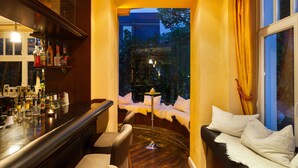 A bar area with a variety of bottles, a round table with a lamp, and a seating area with a view of the outdoors. - Hotel IV Jahreszeiten Kühlungsborn  (Kuehlungsborn)