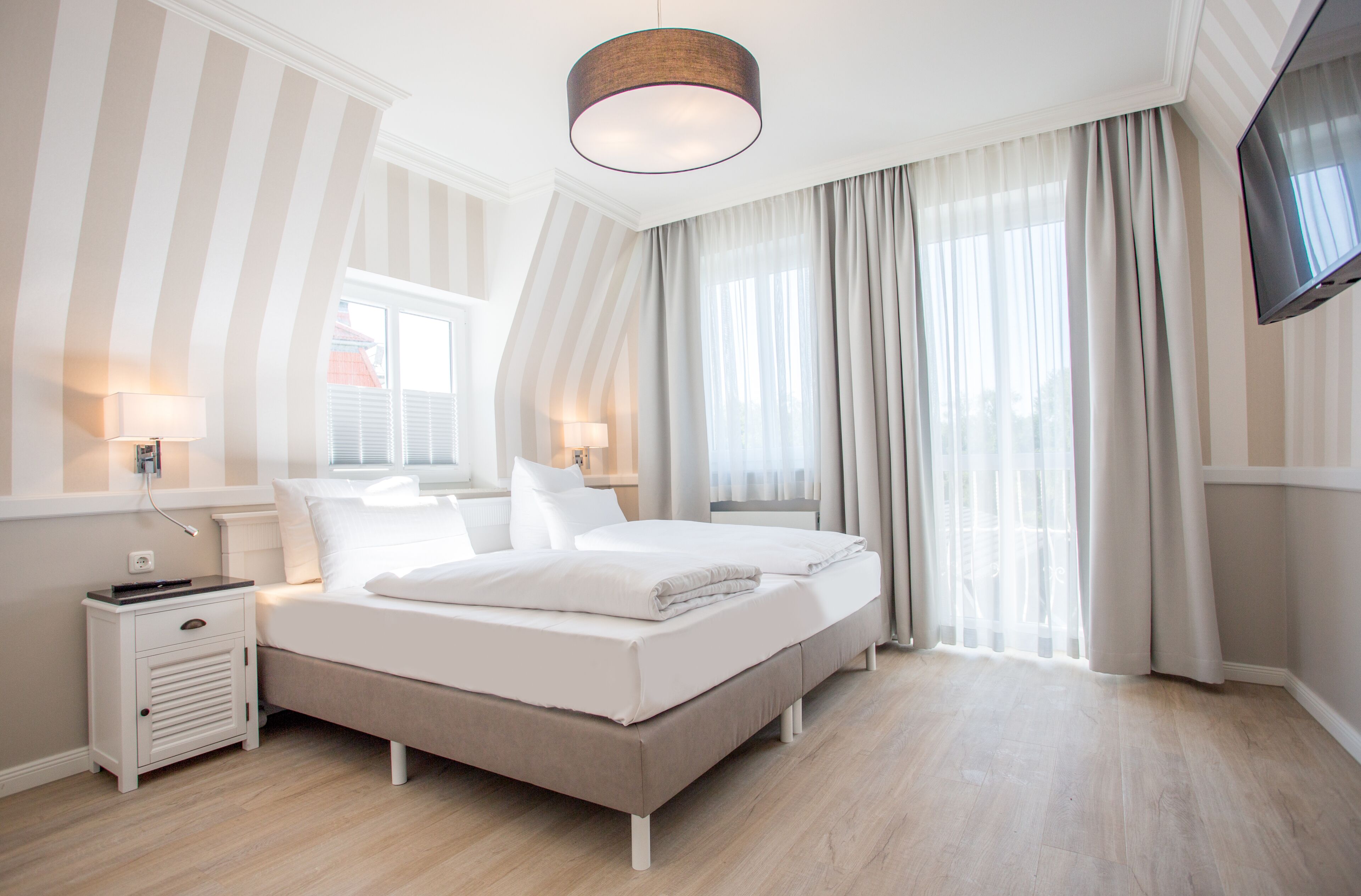 Un dormitorio moderno con una cama grande, dos mesitas de noche, un televisor de pantalla plana y una ventana con cortinas.