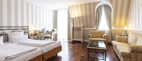 A hotel room with two beds, a desk, a chair, a sofa, and a floor lamp.