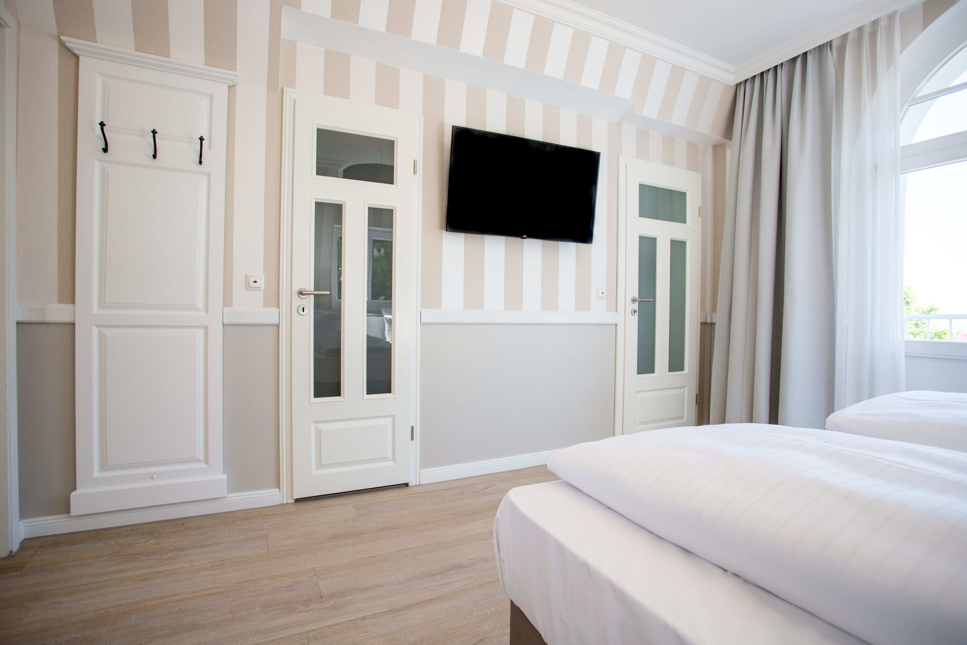 Ein Hotelzimmer mit einem großen Bett, einem flachbildfernseher an der Wand und zwei Türen mit satinierten Glasscheiben.