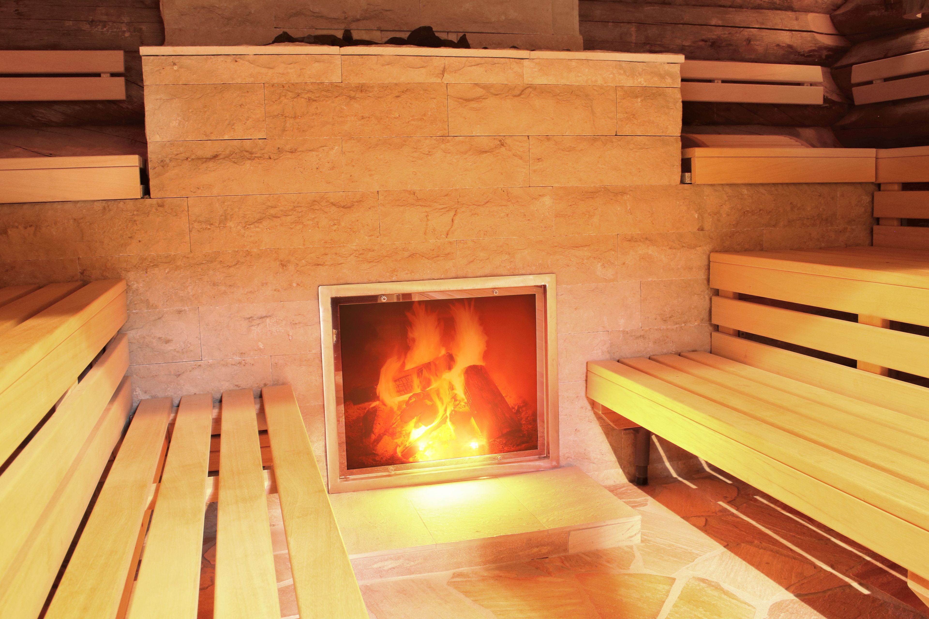 Una chimenea de piedra con fuego, bancos de madera y suelo de baldosas.