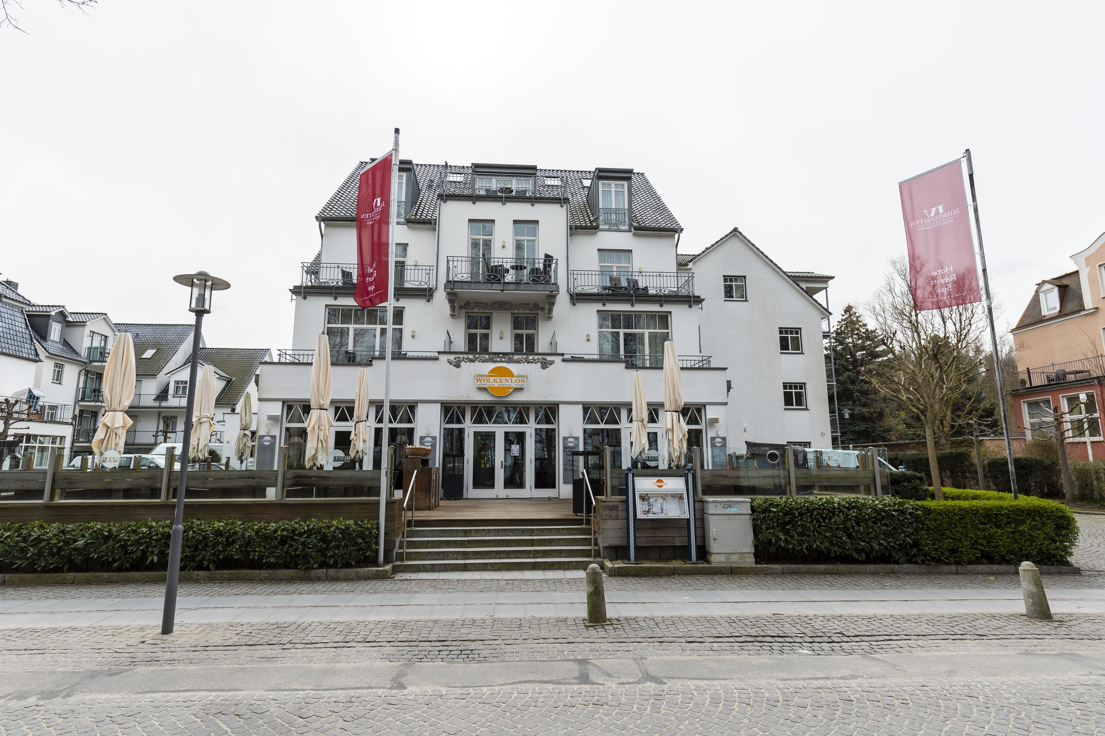 A multi-story building with a balcony, a sign above the entrance, and a flag on the left.