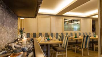 Ein Restaurant mit Sitzboxen und Tischen, eine Bar im Hintergrund sowie eine dekorative Tischdekoration mit Kerzen.
