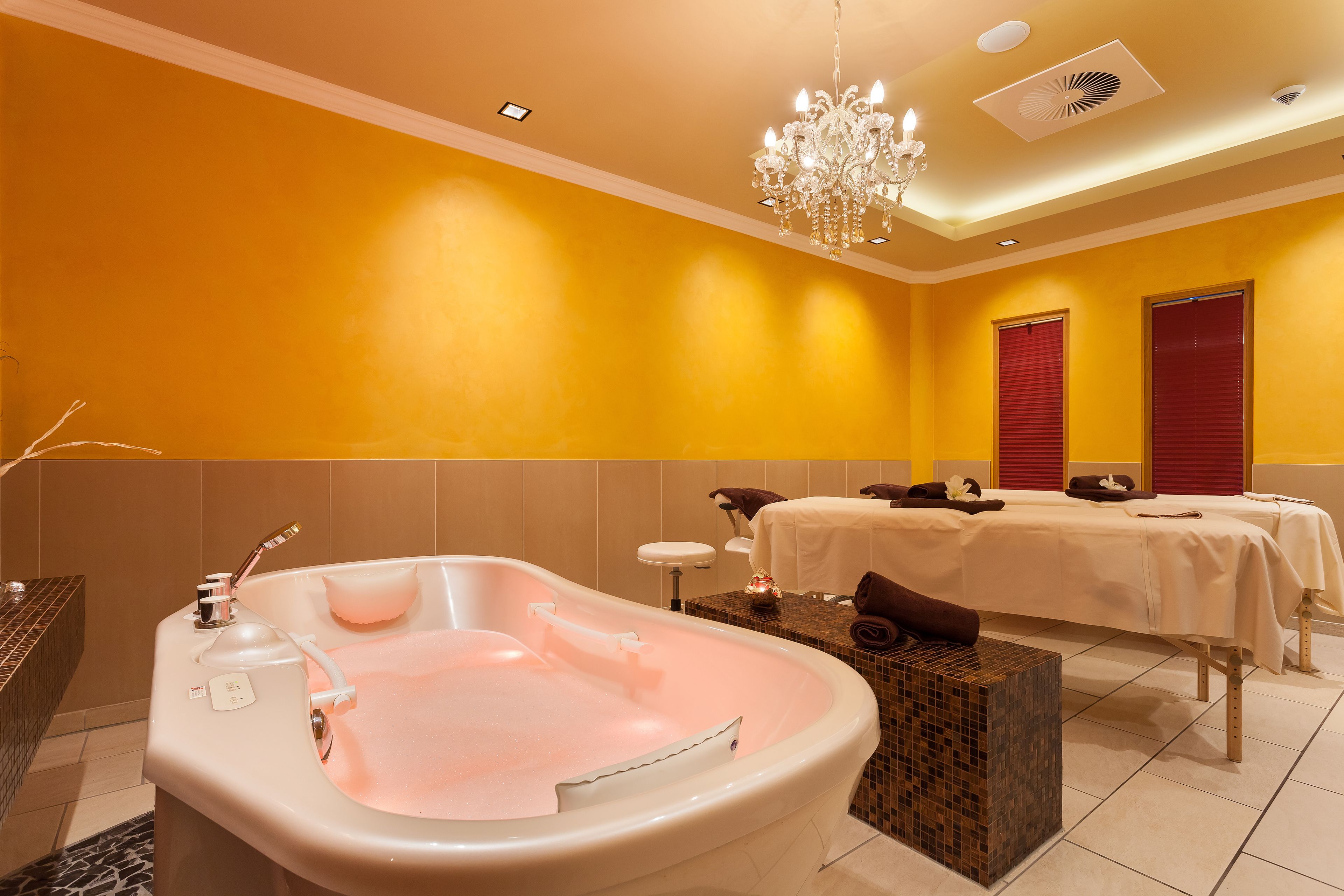 Ein modernes Badezimmer mit einer großzügigen Badewanne, einem Chandelier und einer Massageliege.