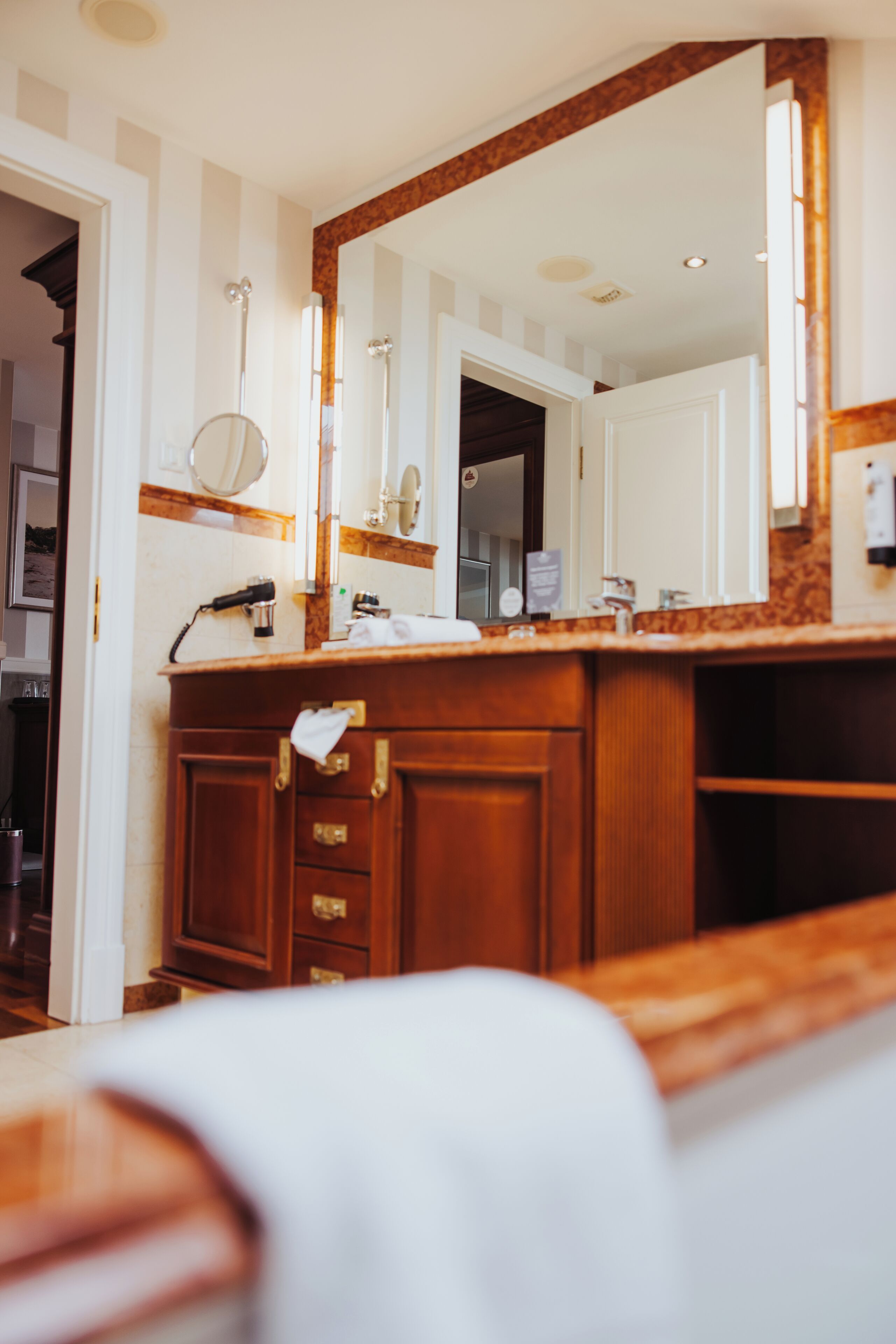 A bathroom with a wooden vanity, a large mirror, and a towel hanging on the door.