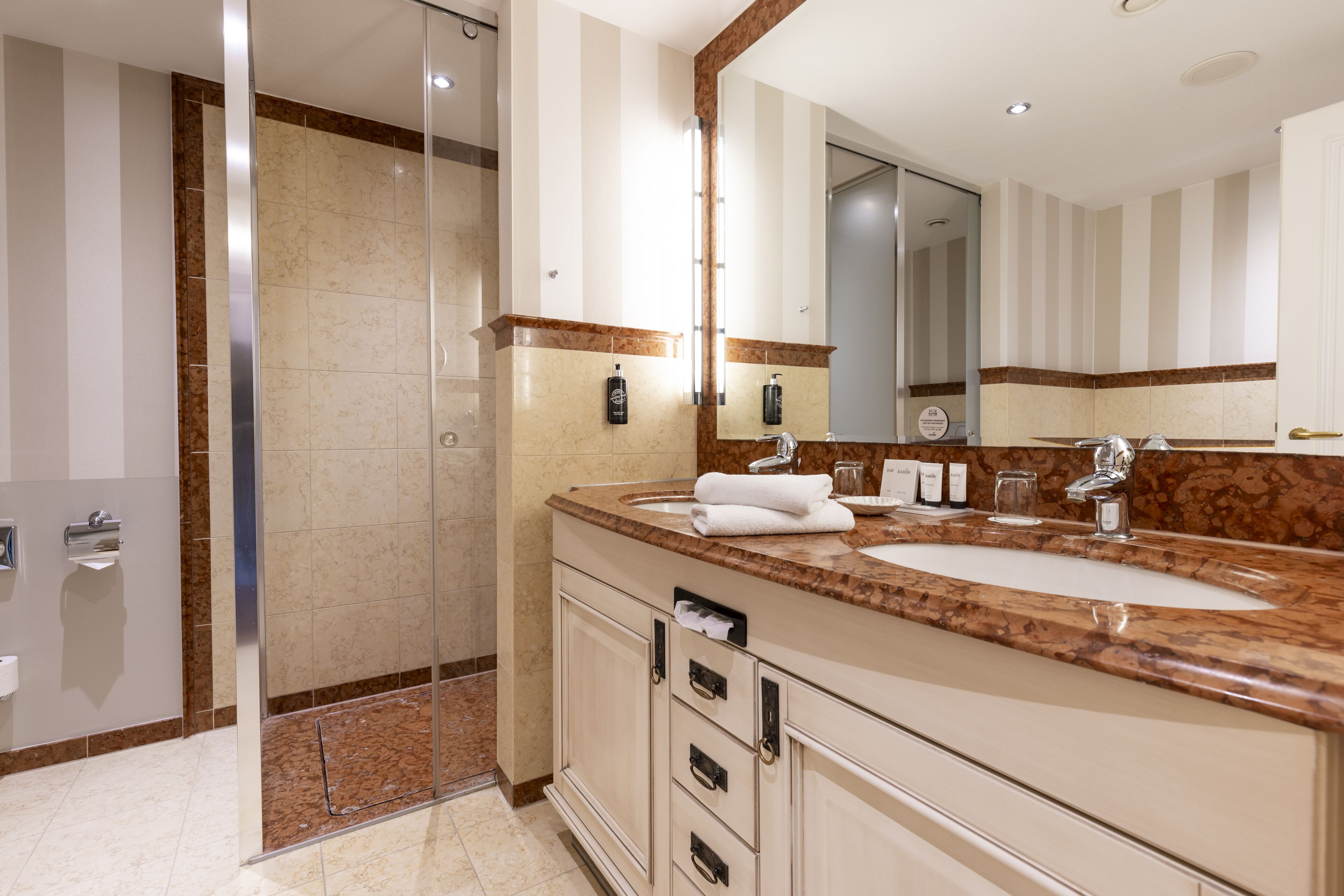 A modern bathroom with a glass shower enclosure, a marble countertop, and a large mirror.