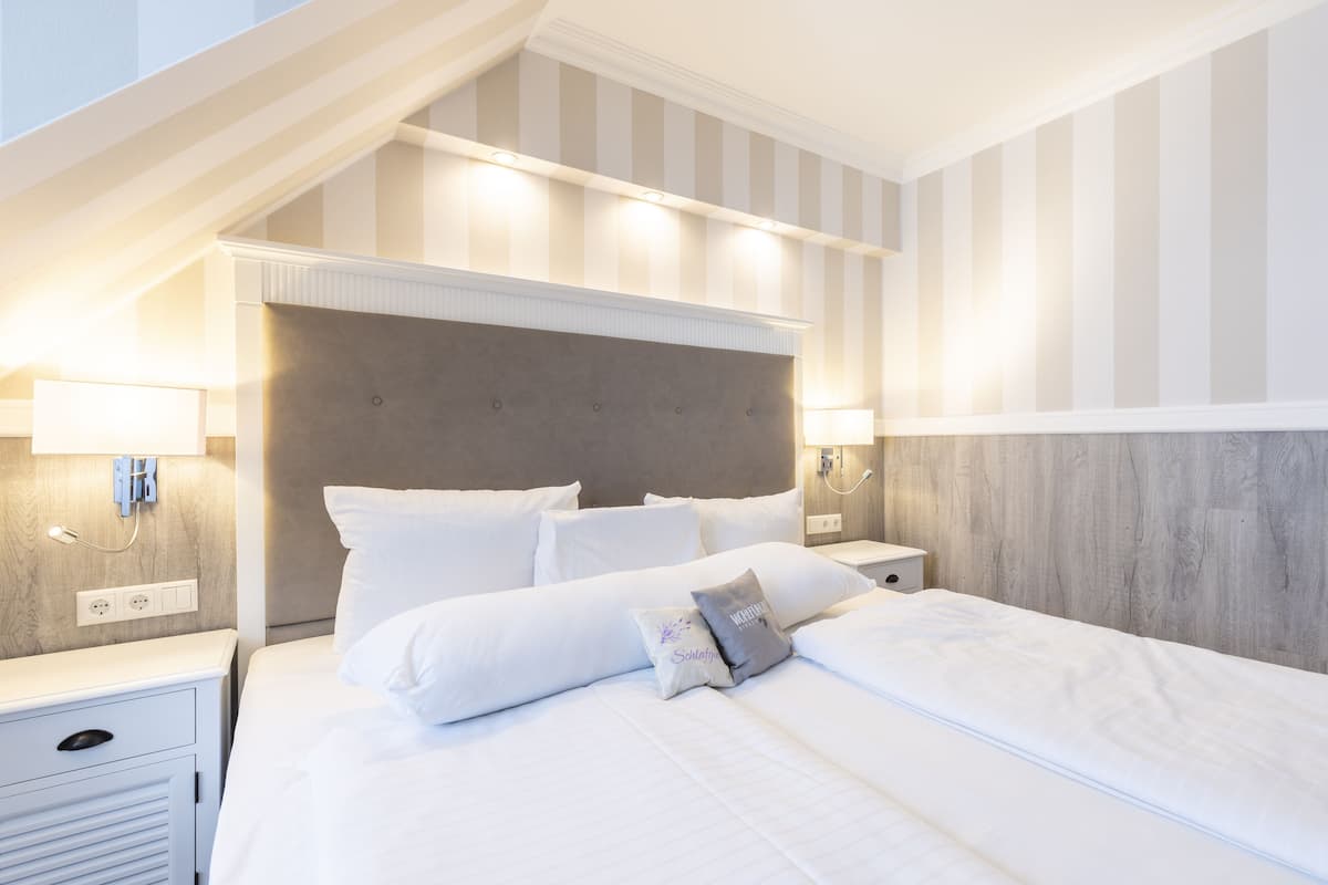 Quarto de hotel com uma cama grande, duas mesas de cabeceira, encosto de cama e parede listrada.