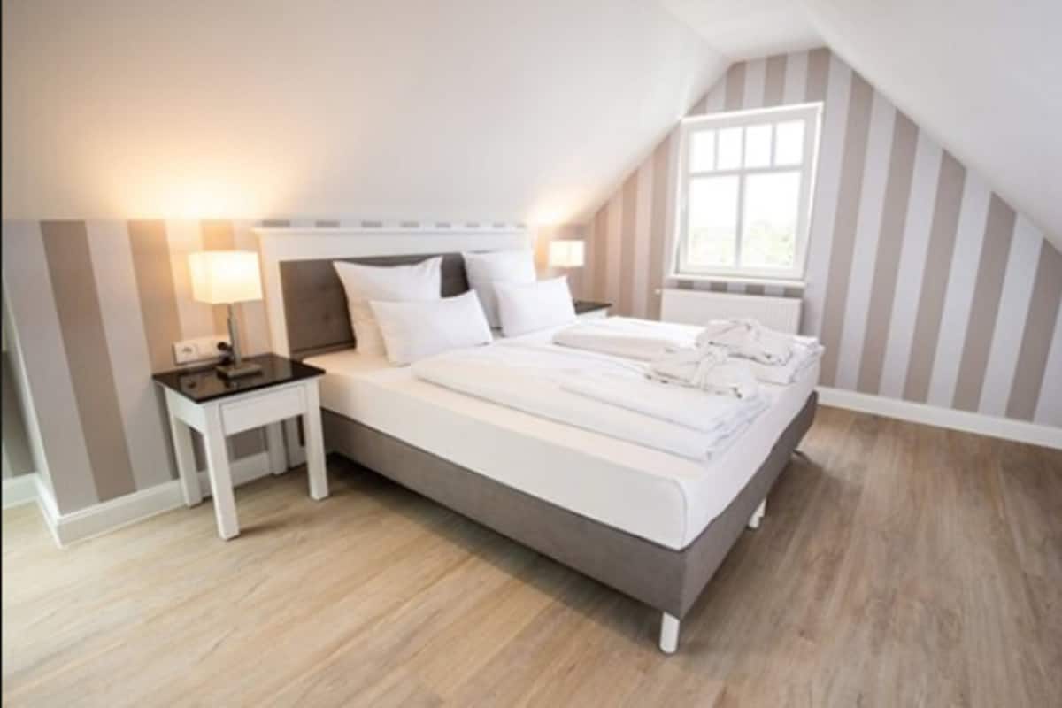 Quarto com cama, mesas de cabeceira, janela e paredes listradas.