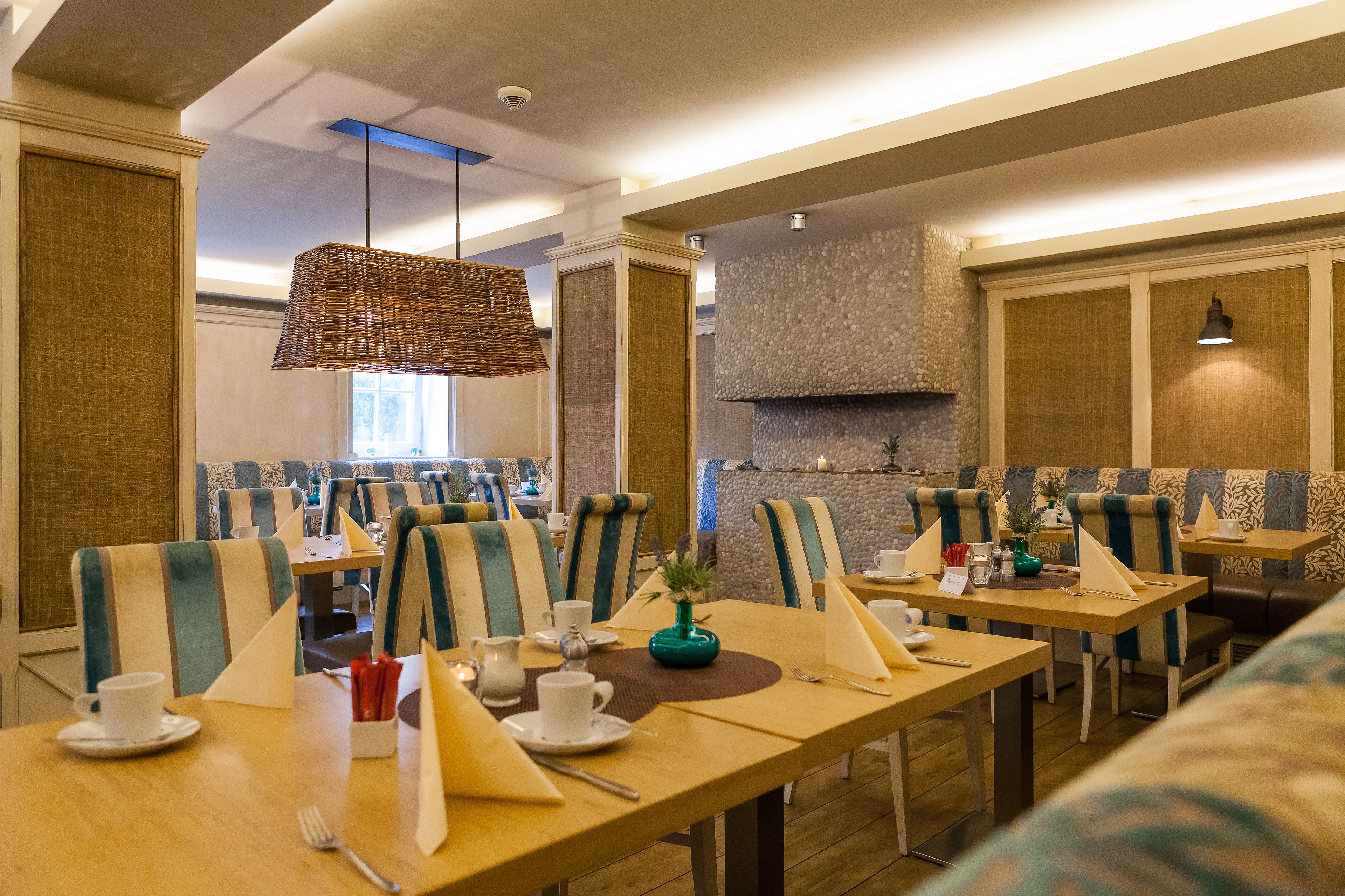 Um restaurante com assentos estofados listrados e mesas retangulares, com louças brancas e um vaso decorativo central.