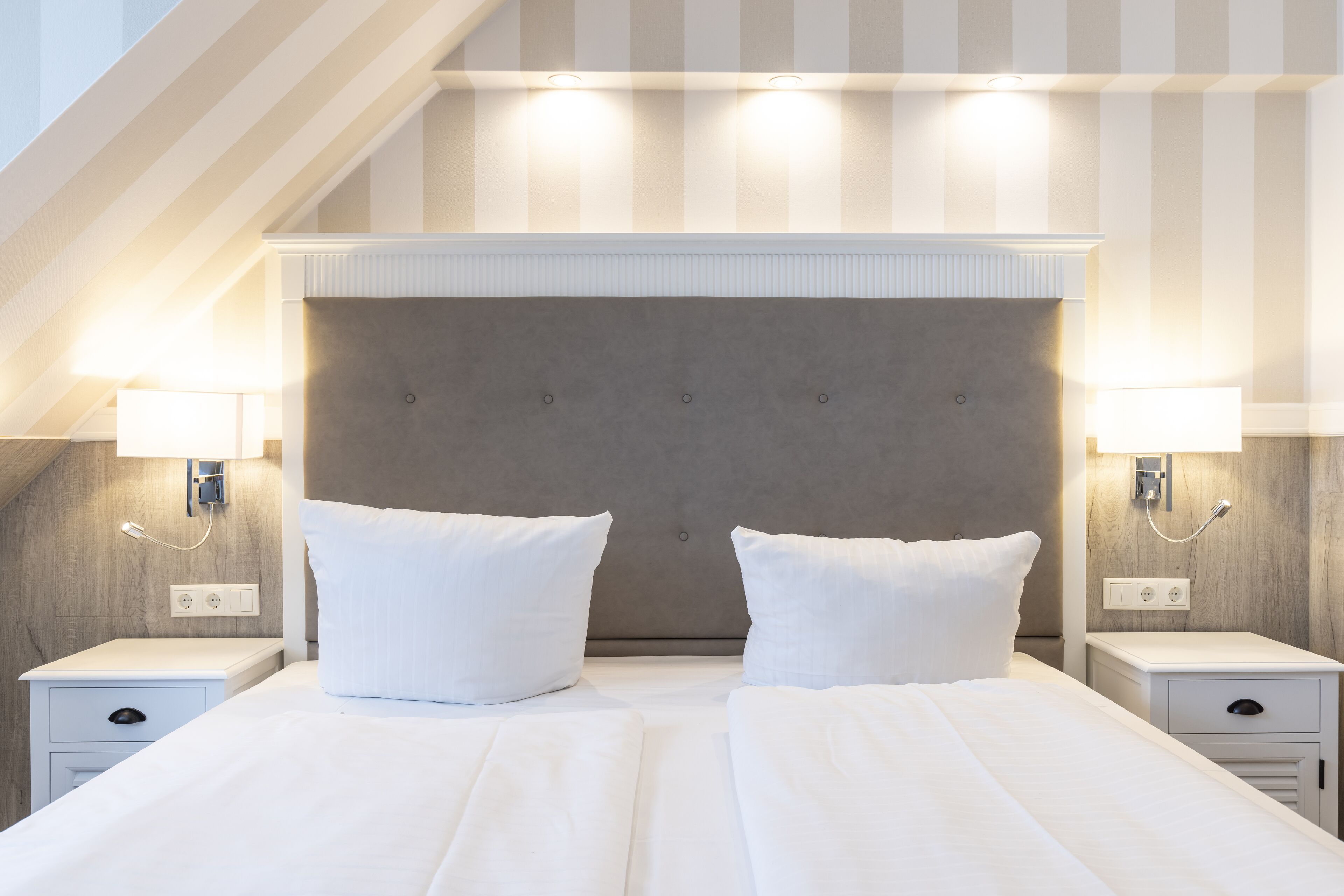 A hotel room with a large bed, two bedside tables, and a headboard with integrated lighting.