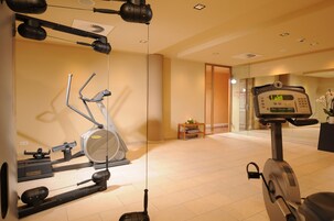 Un gimnasio con equipamiento de ejercicio, una pequeña mesa con una planta y un espejo que refleja la sala.