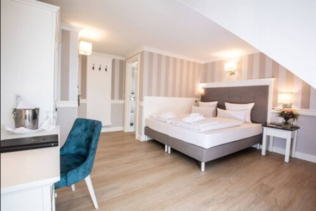 Quarto de hotel moderno com uma cama, uma escrivaninha, uma cadeira e uma pequena mesa com abajur.