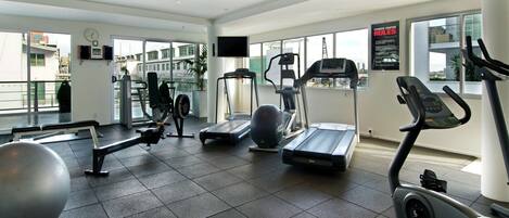A modern gym with various exercise equipment, large windows, and a visible city view.