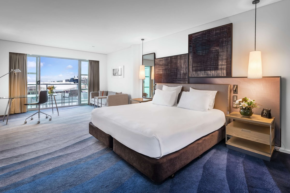 A modern hotel room with a large bed, a desk, and a view of the city.