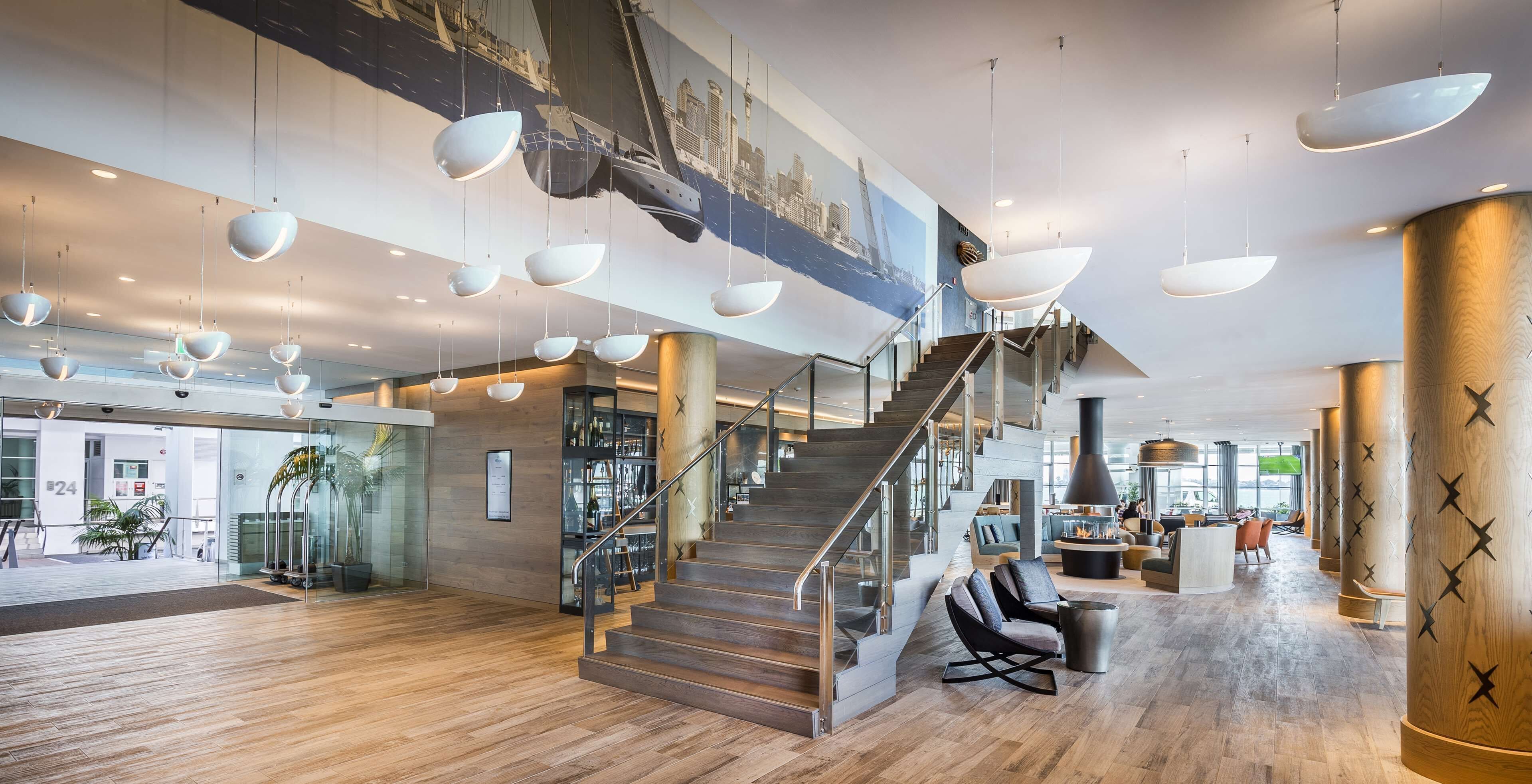 A spacious lobby with a wooden floor, a staircase, and a seating area with modern chairs.