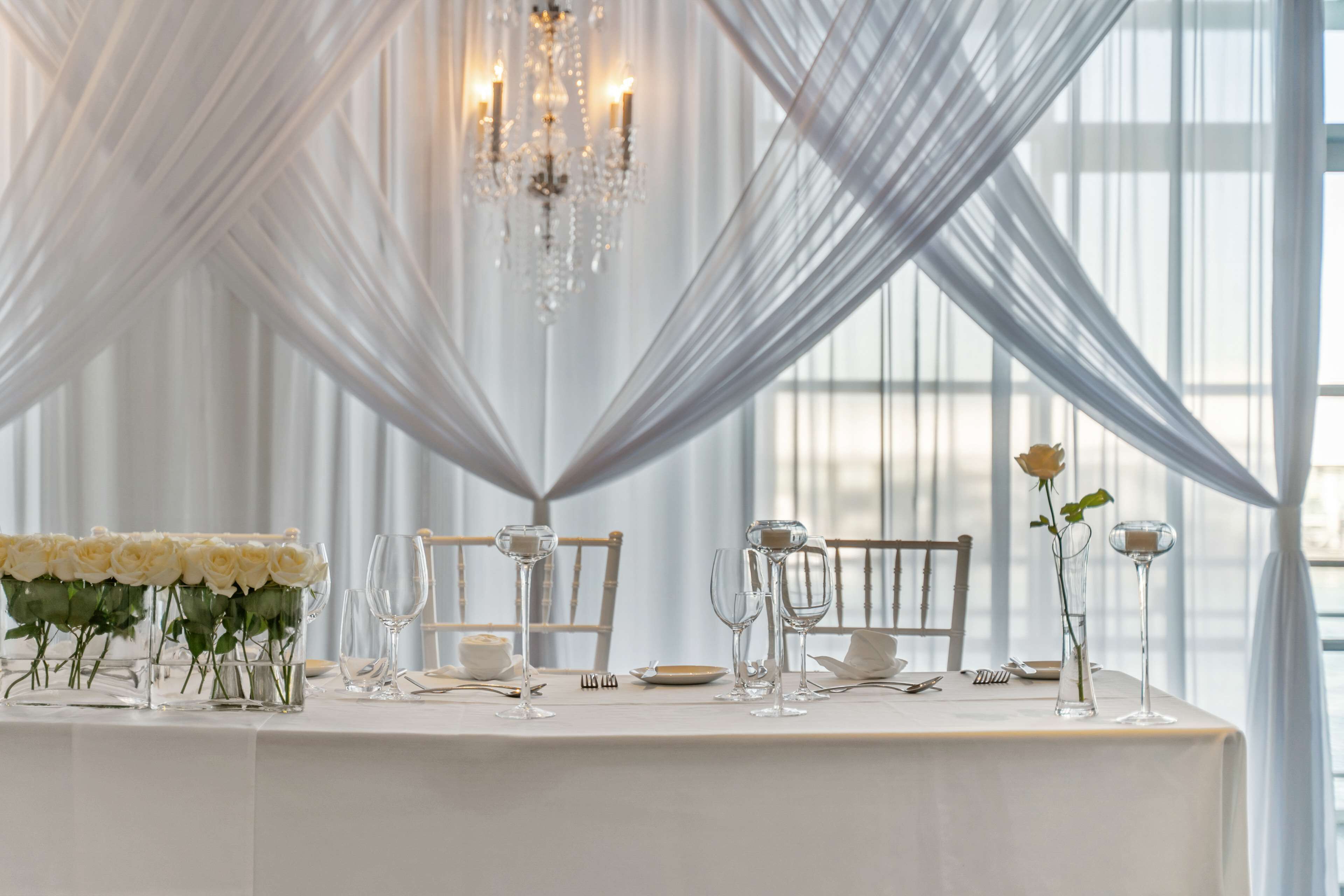 A table set for a formal event with white tablecloth, crystal glassware, and a bouquet of white roses.