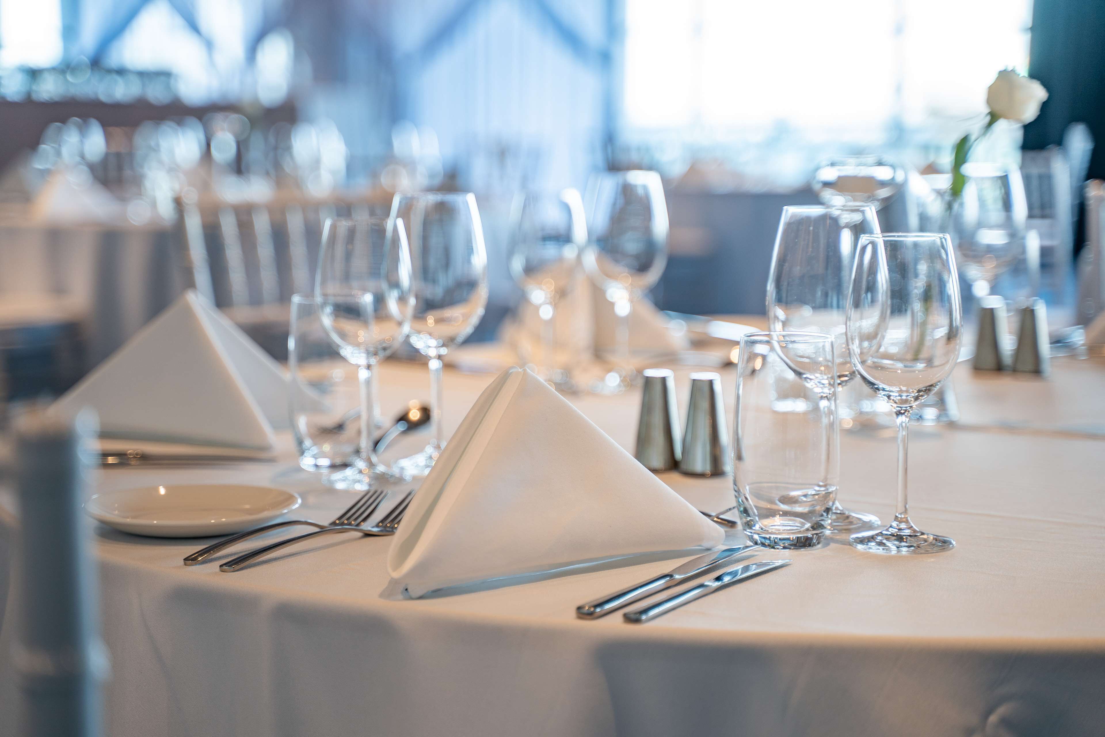 Una mesa elegantemente dispuesta con manteles blancos, copas brillantes y cubiertos, preparada para una cena formal.