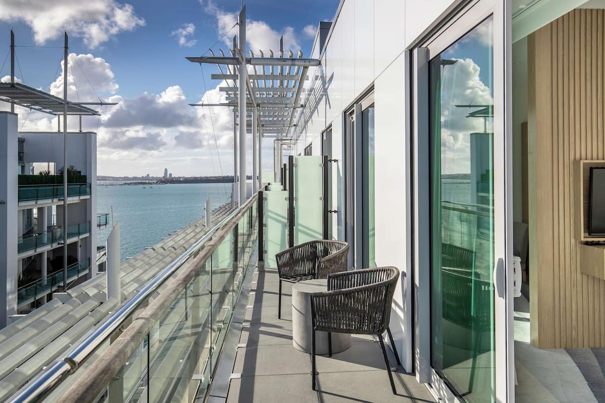 A modern balcony with glass railings, wicker chairs, and a view of the sea.