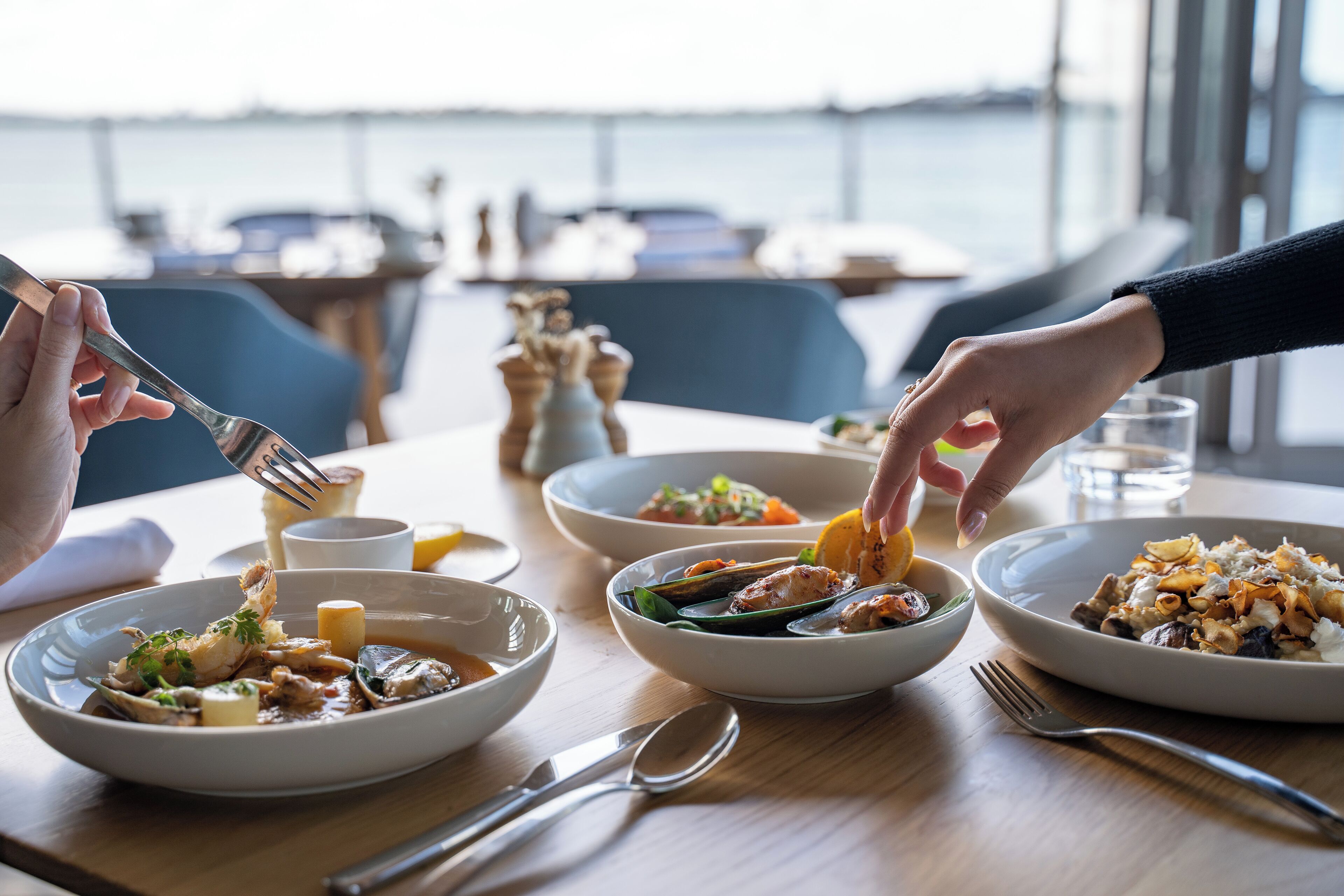 A dining table with multiple plates of seafood dishes, utensils, and a glass of water.