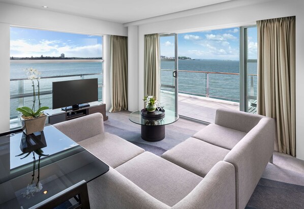 A modern hotel room with a large balcony, a glass table, a sofa, and a TV.