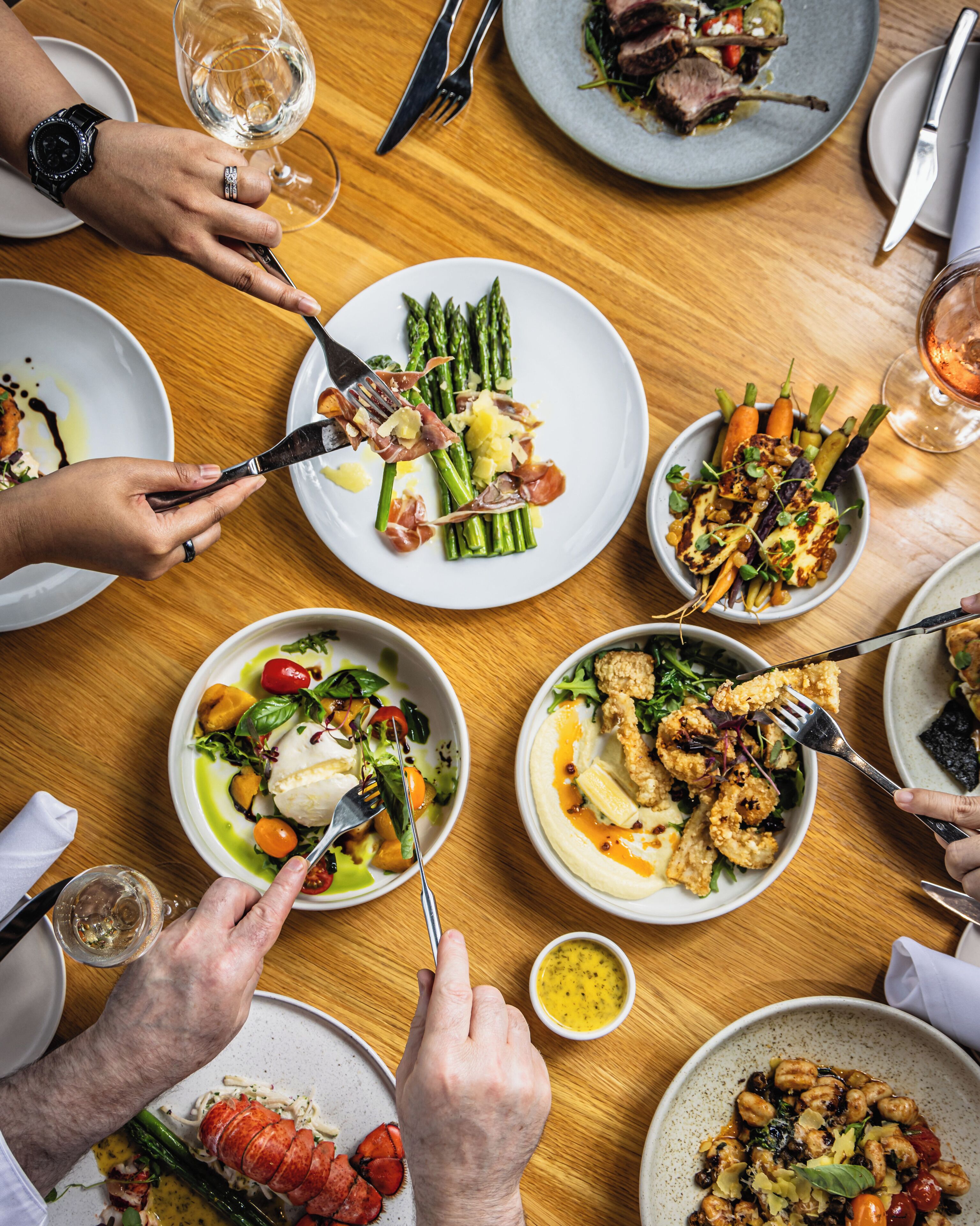 A group of people dining at a wooden table with various dishes, including seafood and vegetables.