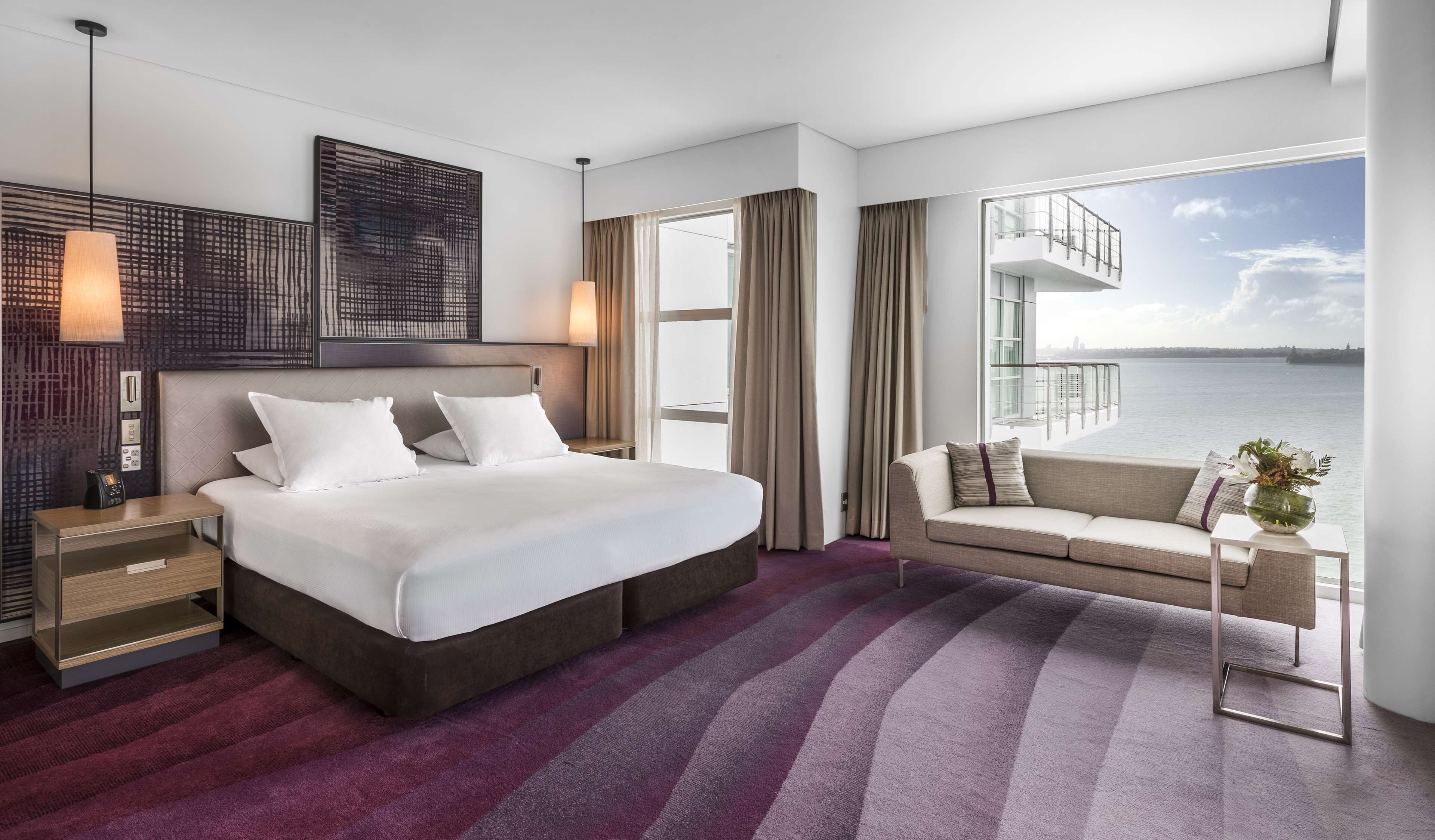Habitación de hotel moderna con una cama grande, un sofá, vista al agua y un balcón.