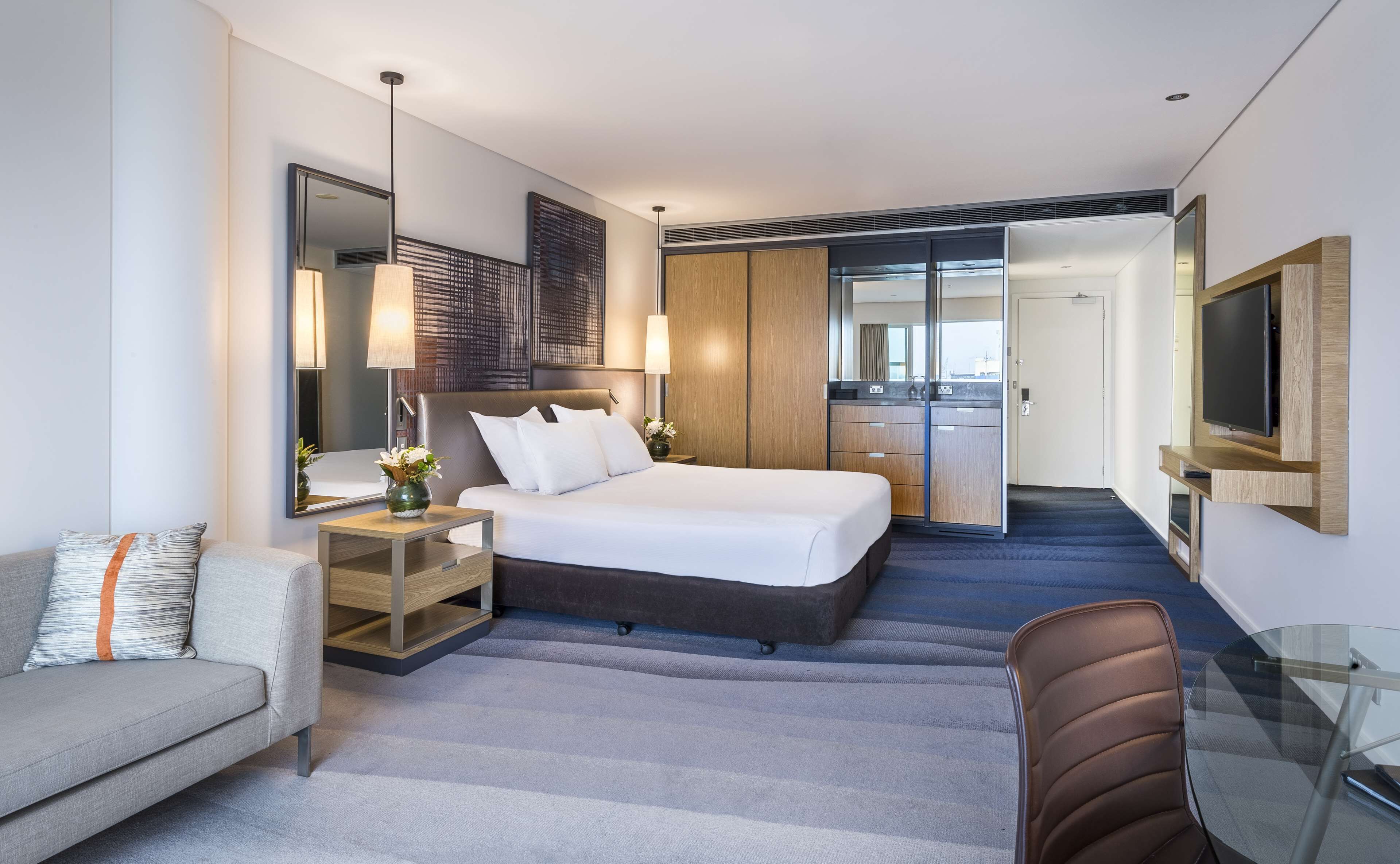 Habitació d'hotel moderna amb llit, sofà, escriptori, televisió i petita cuina.
