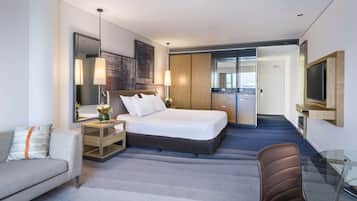 Habitació d'hotel moderna amb llit, sofà, escriptori, televisió i petita cuina.