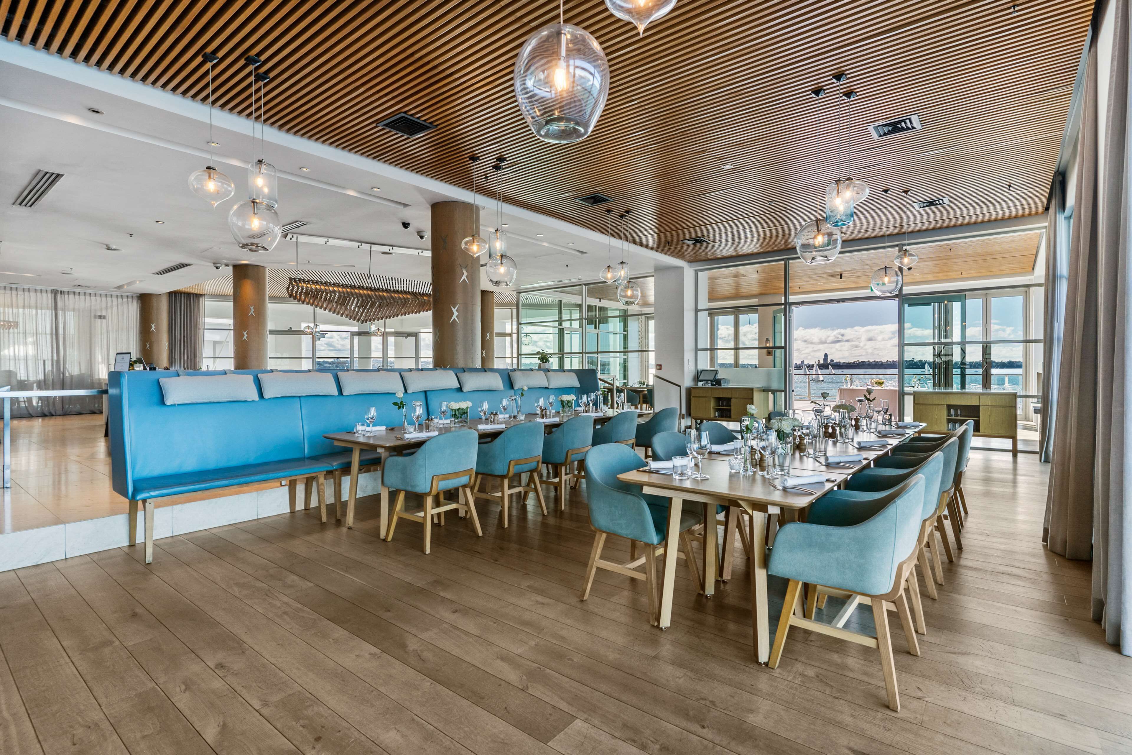 A modern restaurant with wooden floors, blue seating, and large windows offering a view.