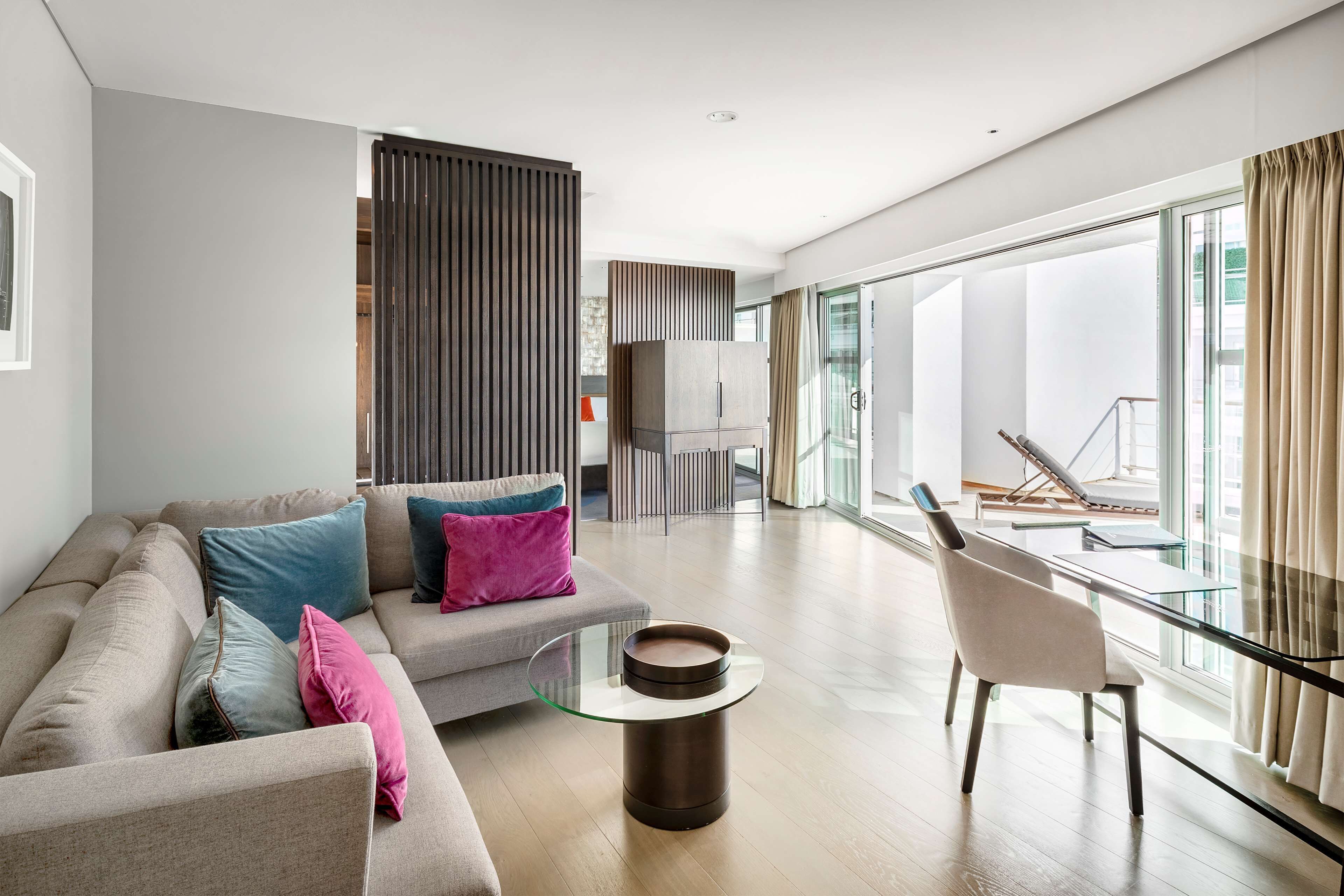 A modern living room with a sofa, a glass coffee table, and a view of the outdoors.