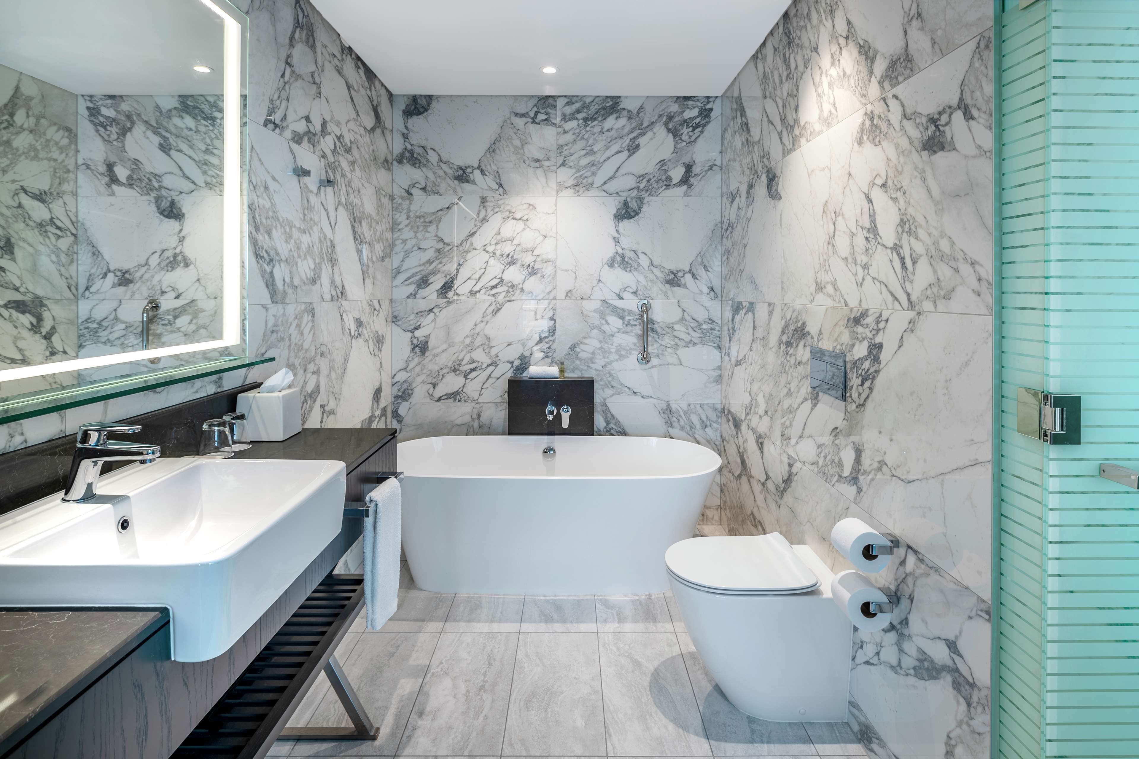 A modern bathroom with a marble wall, a freestanding bathtub, a sink, and a toilet.