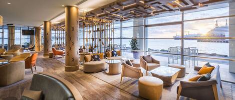 A spacious lounge area with large windows offering a view of the water and a ship.