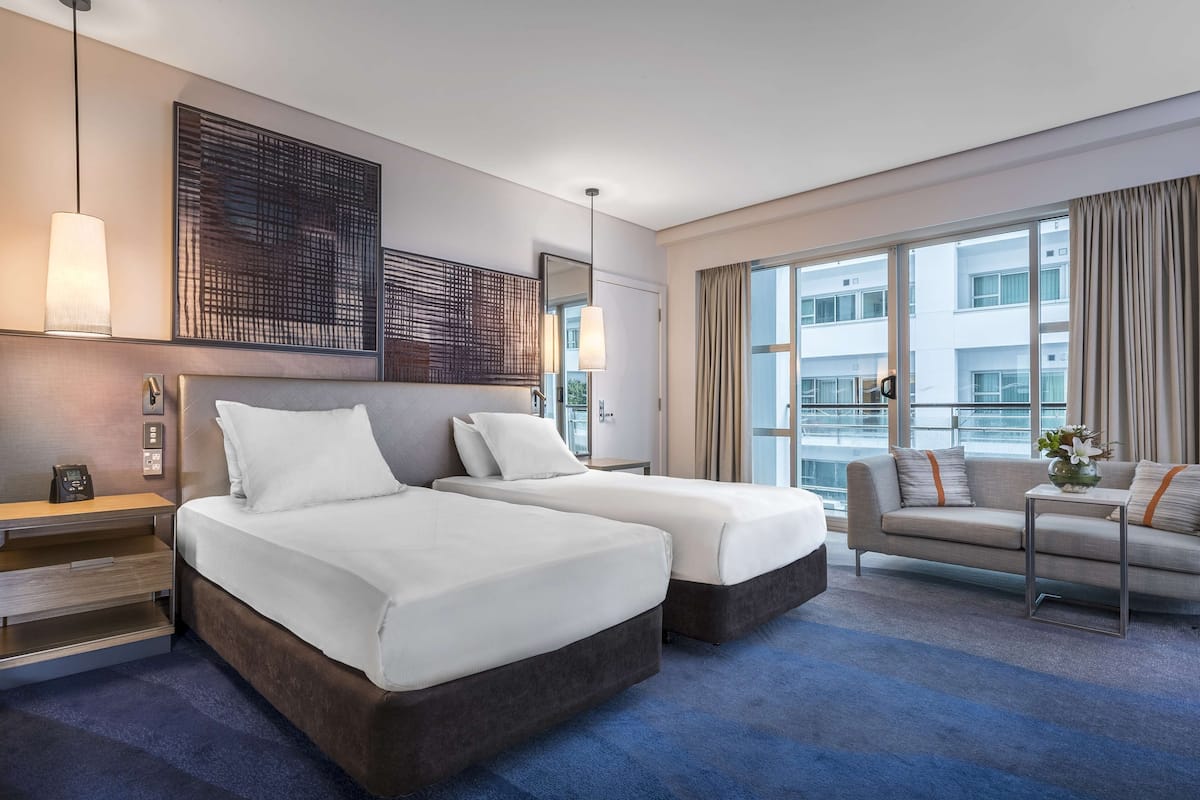 A hotel room with two beds, a sofa, a desk, and a large window.