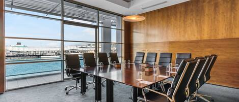 A conference room with a large table, multiple chairs, and a view of a body of water through large windows.