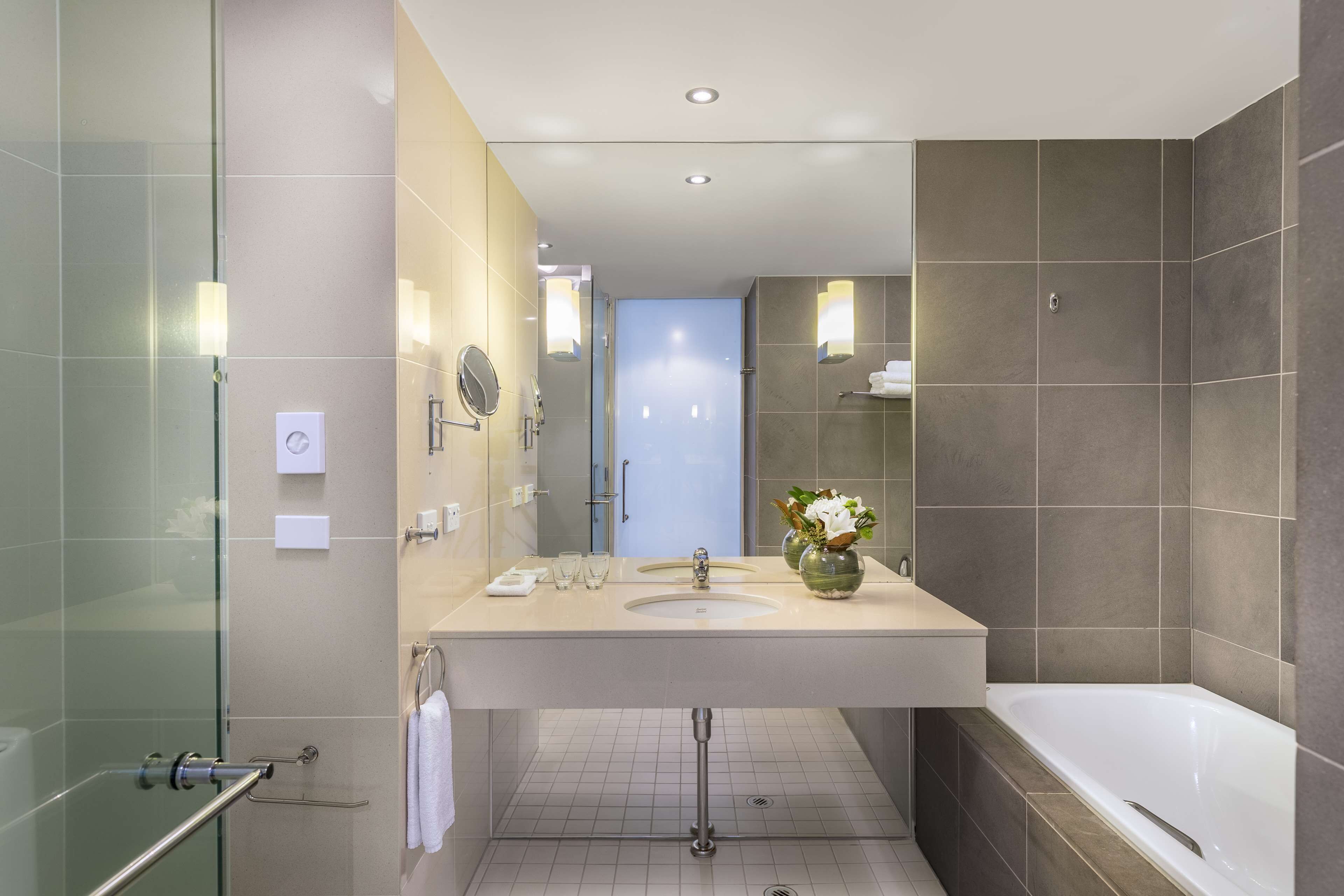 A modern bathroom with a glass shower enclosure, a large sink with a mirror, and a bathtub.