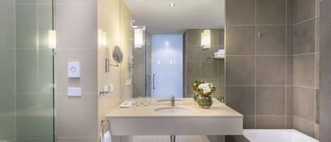 A modern bathroom with a glass shower enclosure, a large sink with a mirror, and a bathtub.