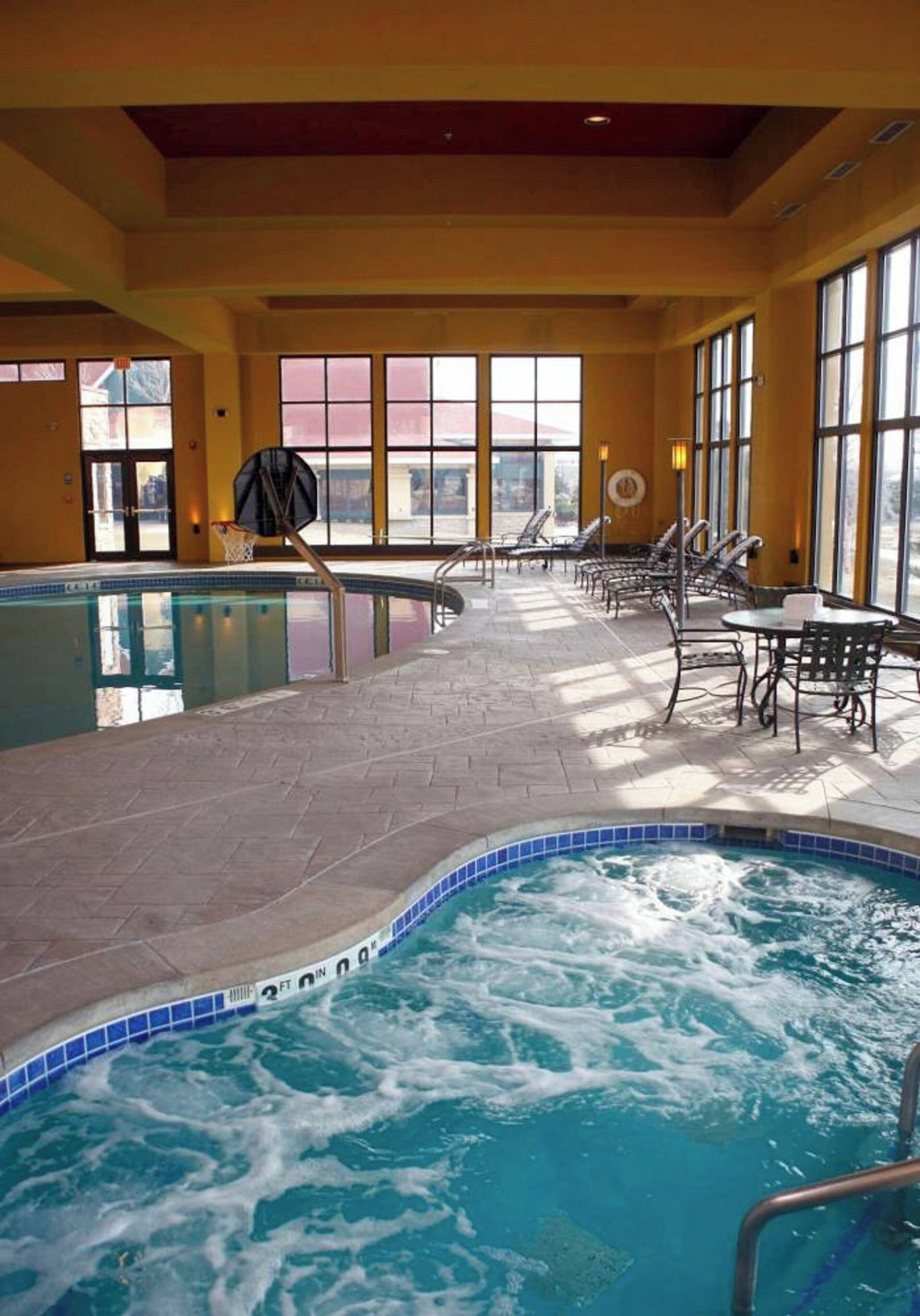 Piscina interna com hidromassagem, área de estar iluminada pelo sol e um aro de basquete.