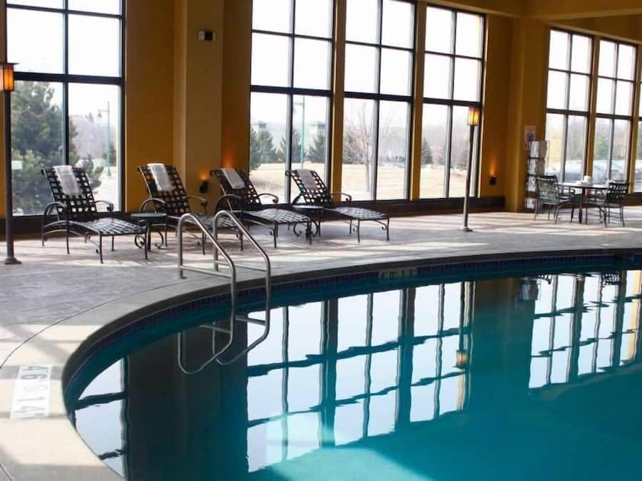 A pool area with lounge chairs and a table, large windows, and a clear view of the outdoors.