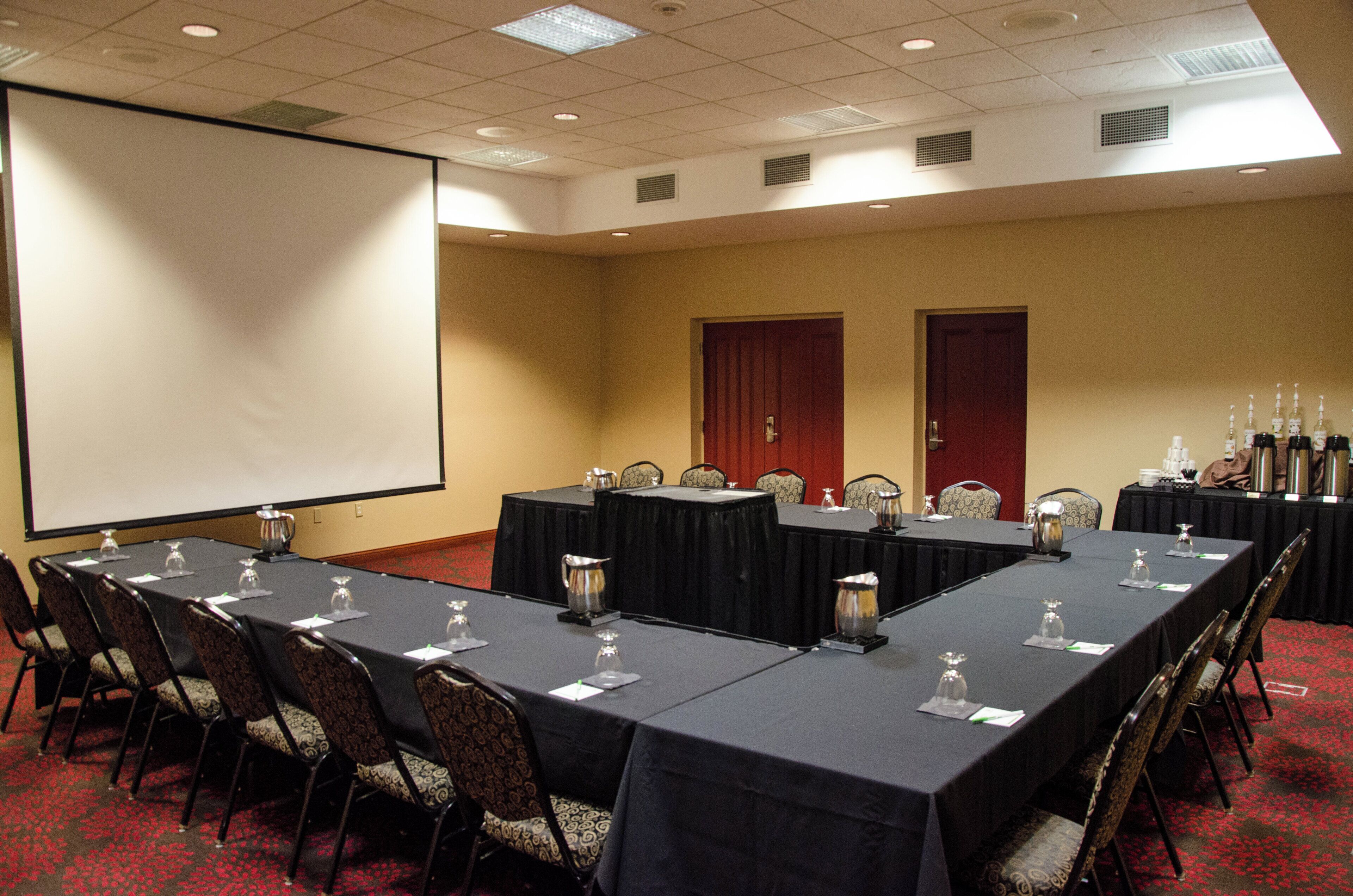 A conference room with a large screen, multiple tables with chairs, and a red carpeted floor.