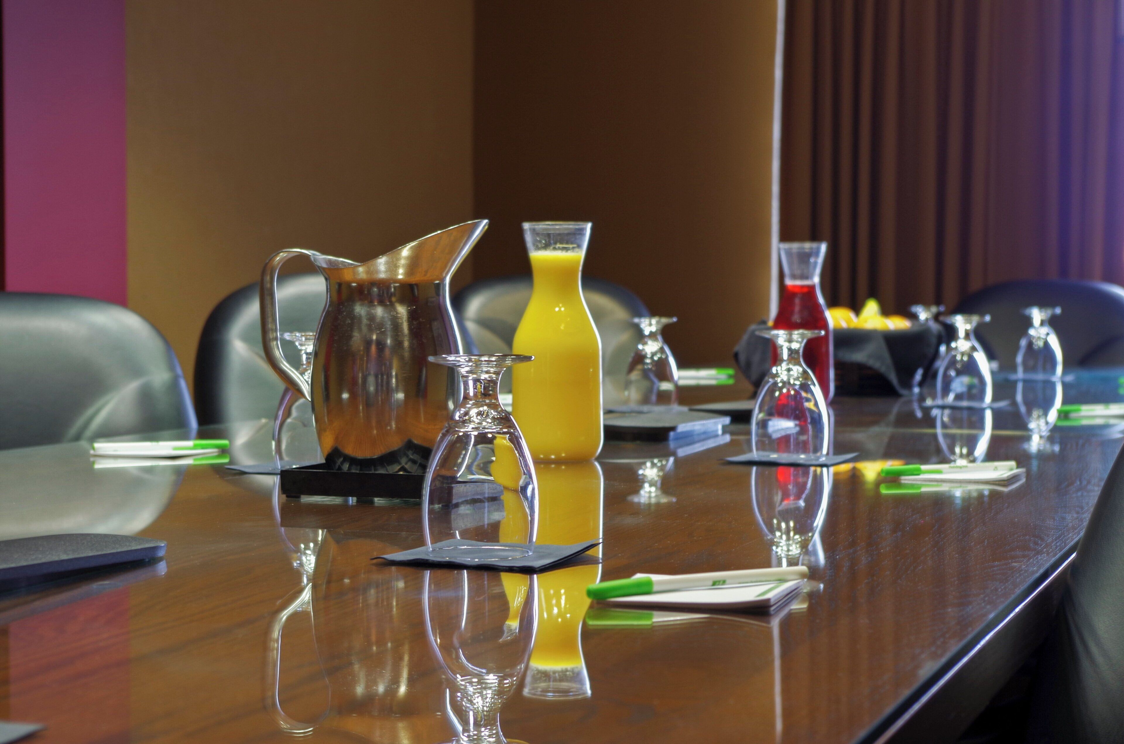 A conference table with various glassware, including a pitcher, a carafe, and a glass with a yellow liquid.